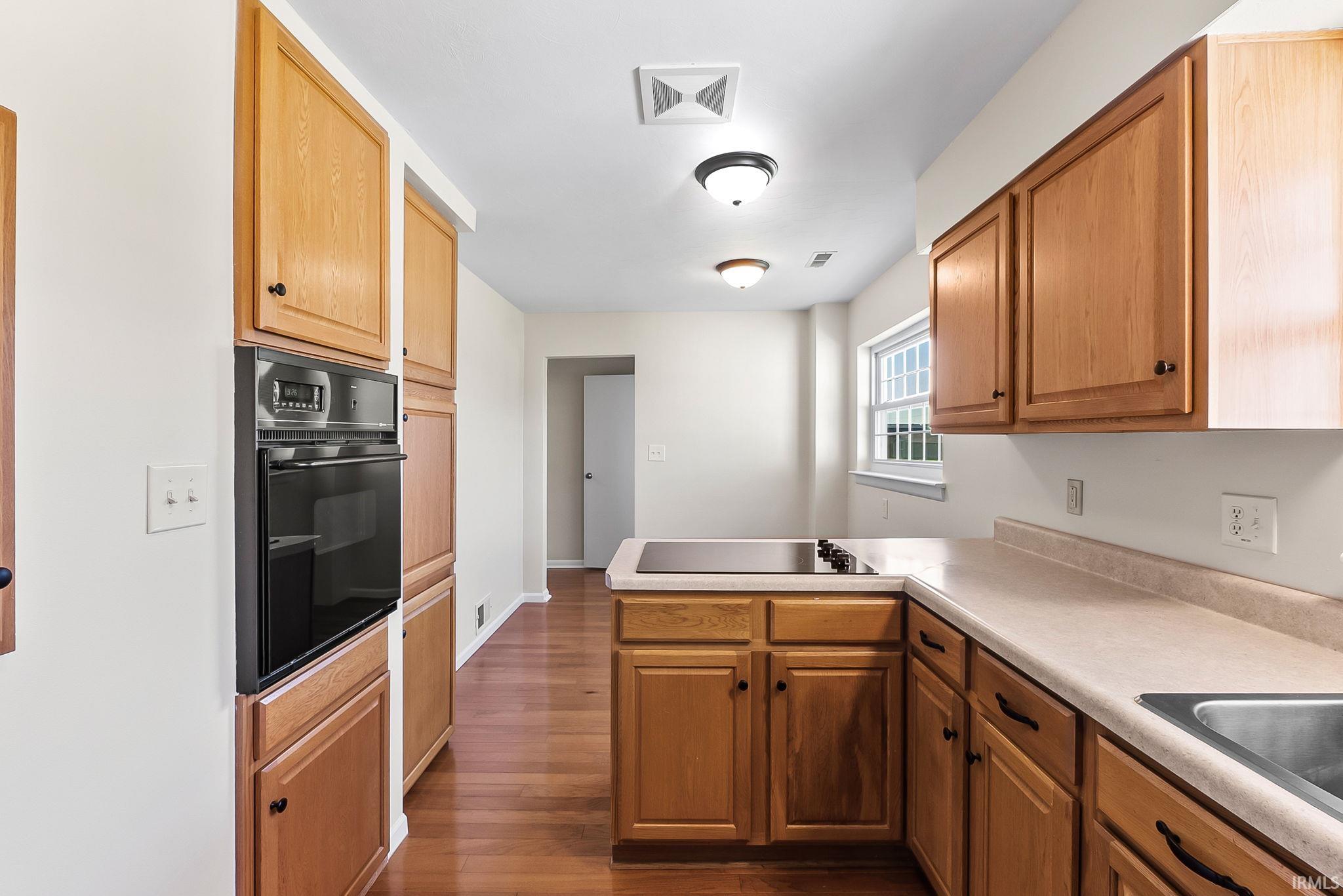 Kitchen featuring wood-finish cabinetry, light-toned countertops, a built-in oven, and a cooktop