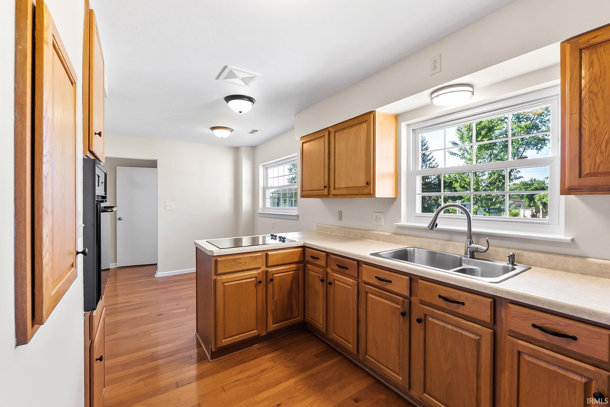 Kitchen featuring wood-finish cabinetry, a double basin stainless steel sink, and a built-in cooktop