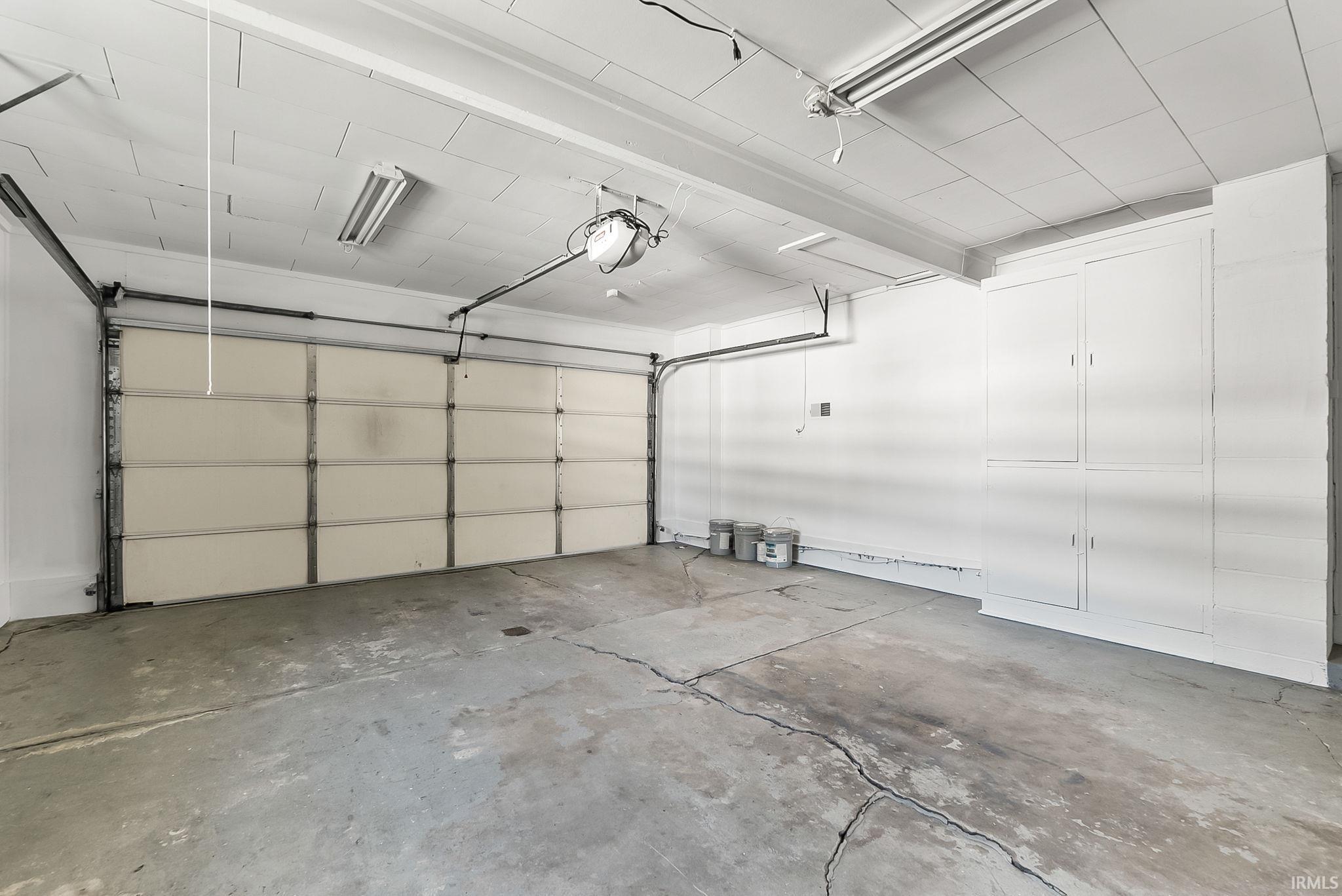 Spacious garage featuring a concrete floor, built-in storage cabinetry, fluorescent lighting, and an automatic garage door opener