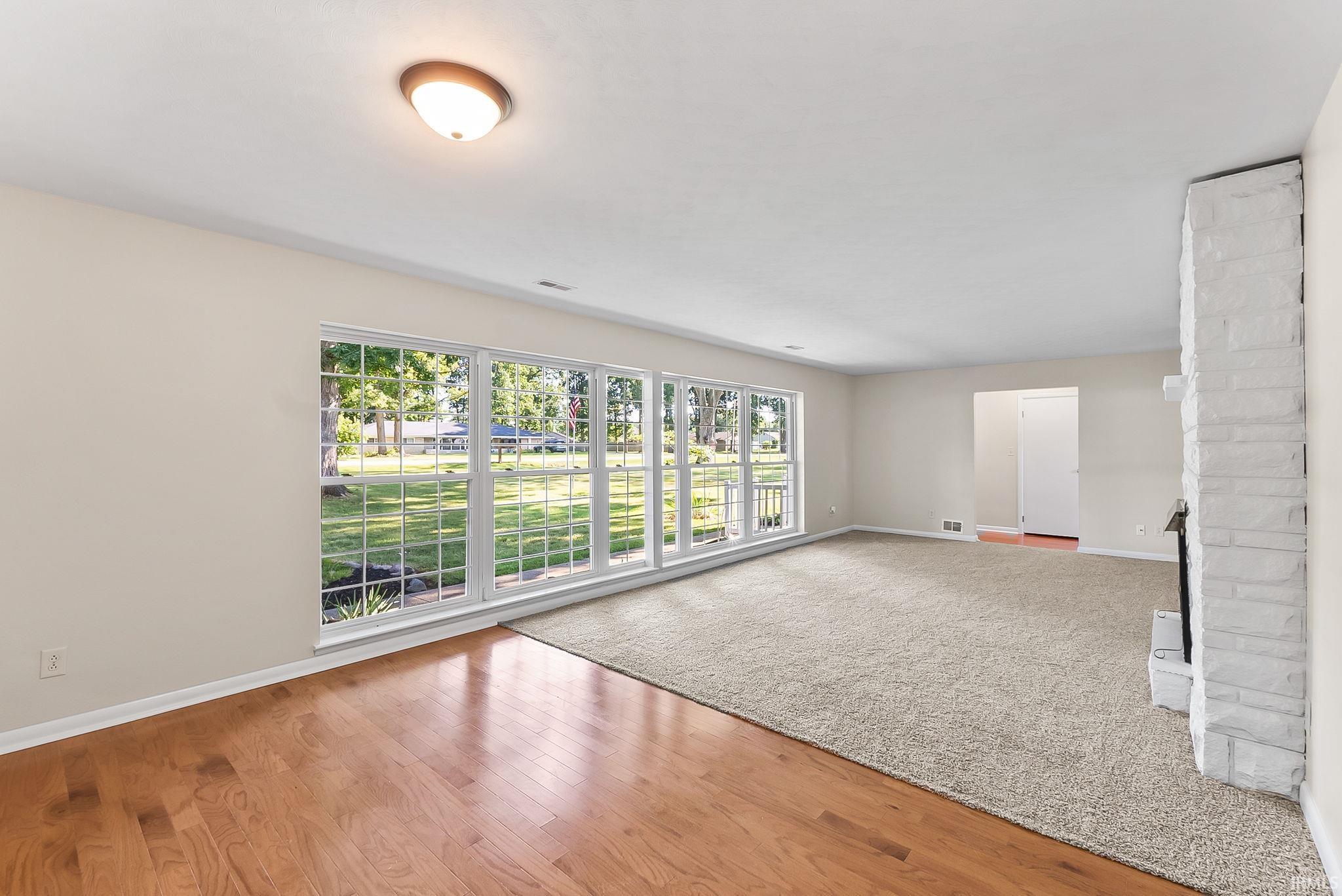 Expansive windows, light wood-finish flooring, neutral wall tones, and a stone-clad fireplace