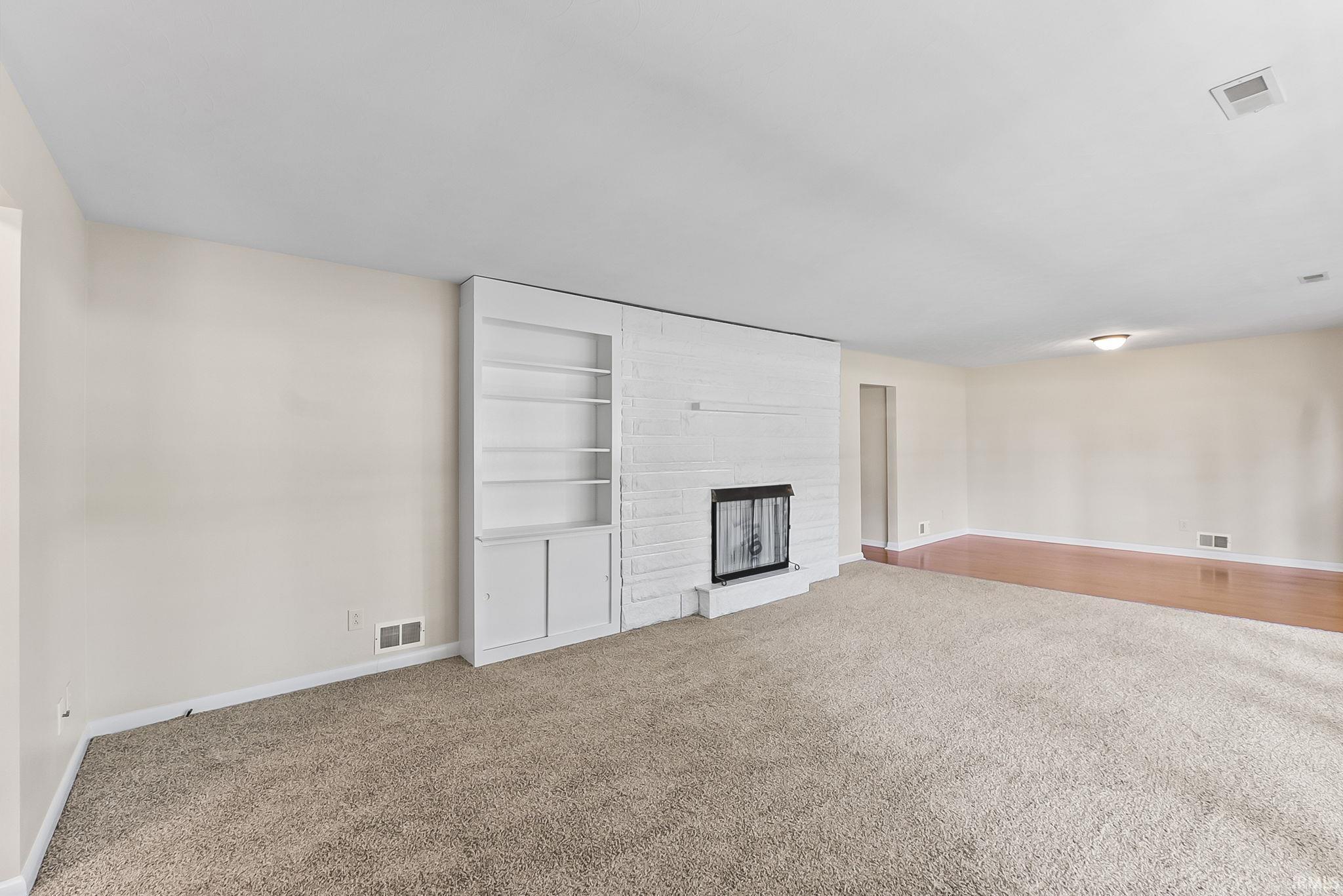 Carpeted flooring complemented by a white brick fireplace with a metal screen