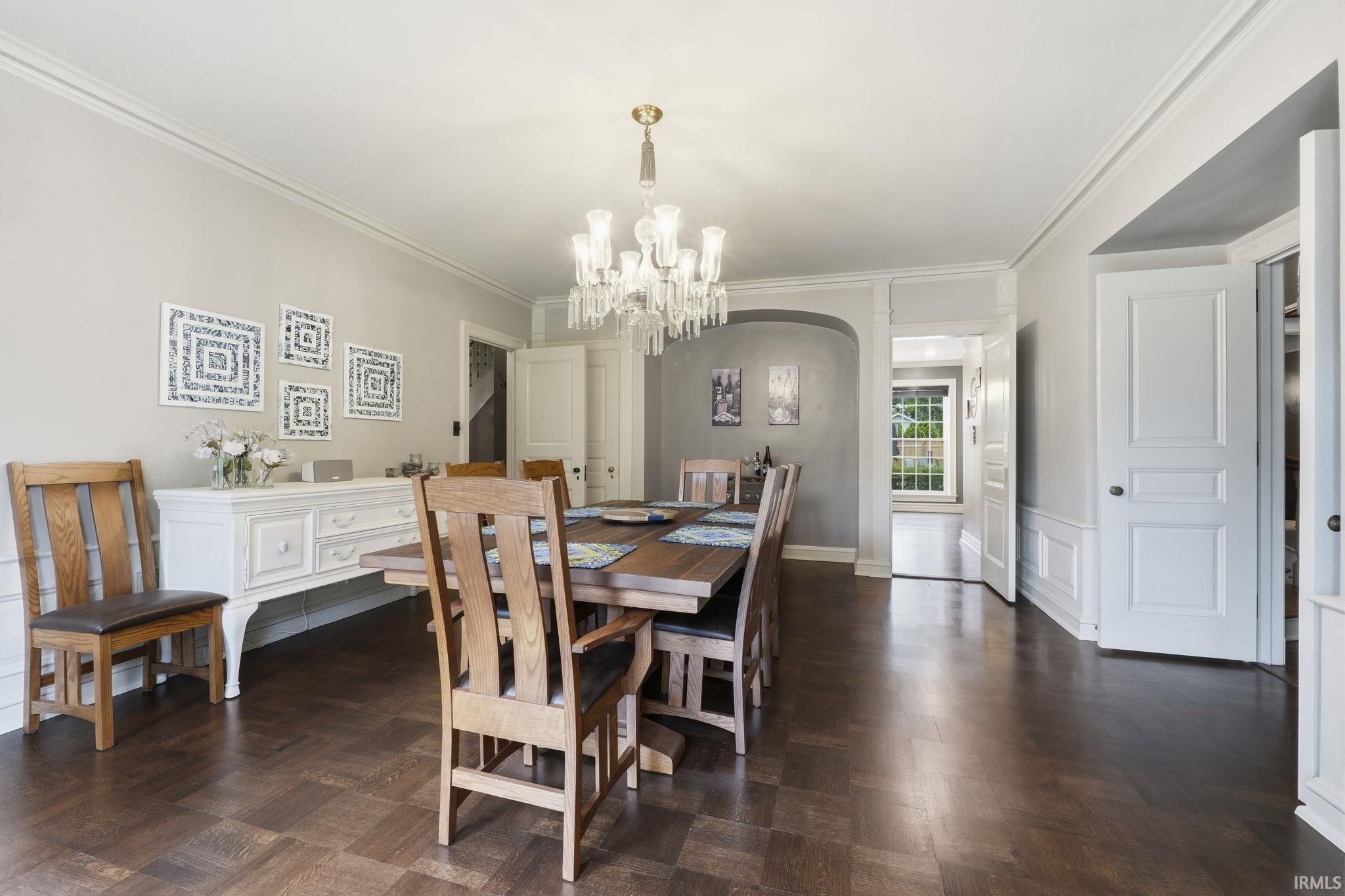 Chandelier lighting illuminates the dining area with crown molding, wainscoting, and wood-finish flooring