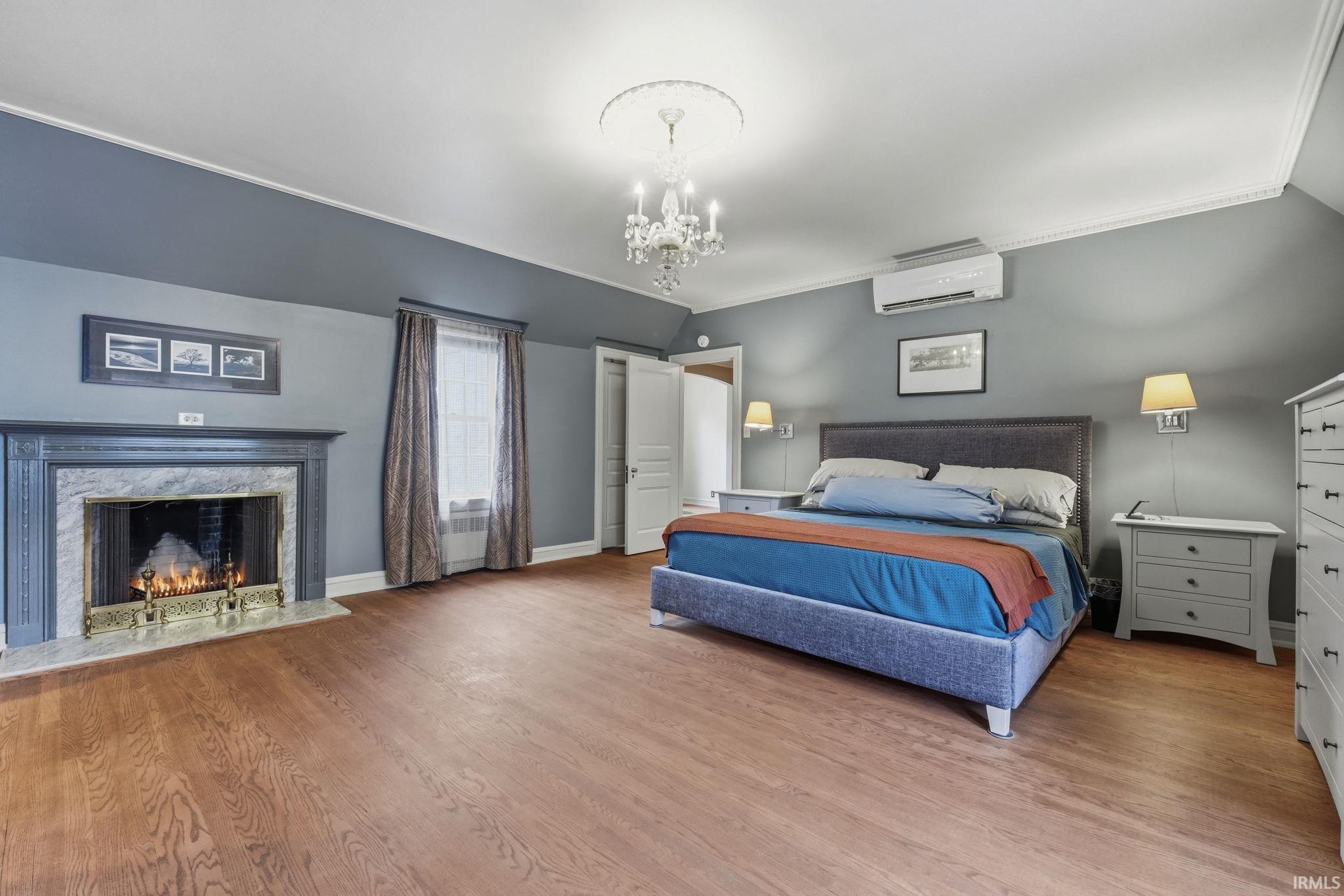 Wood-finish flooring, a decorative fireplace with a stone surround, crown molding, and a chandelier