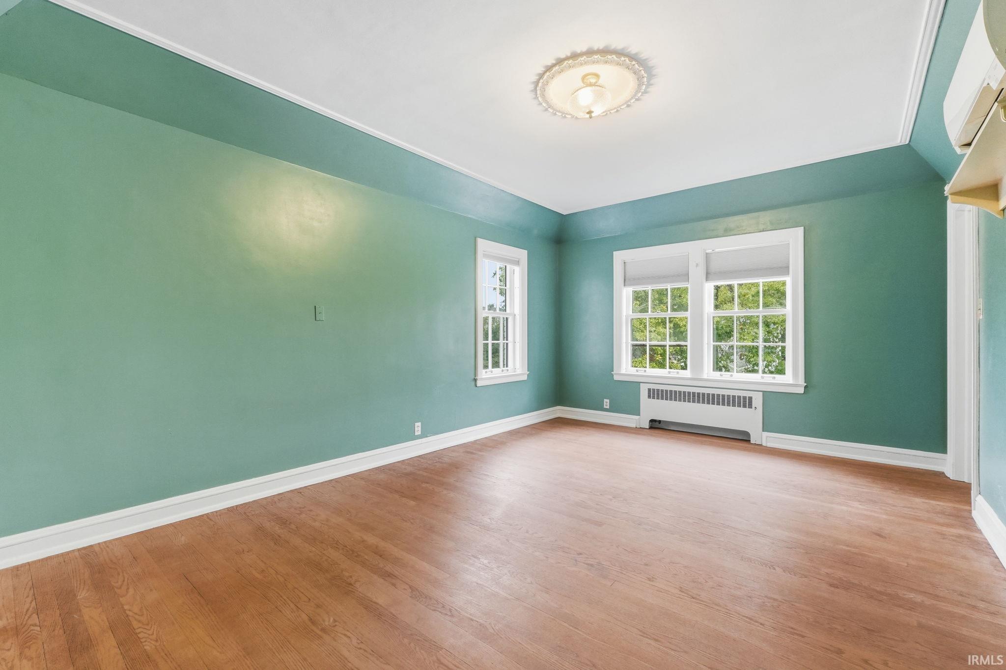 Wood-finish flooring, two window units, and a ceiling light fixture with decorative molding