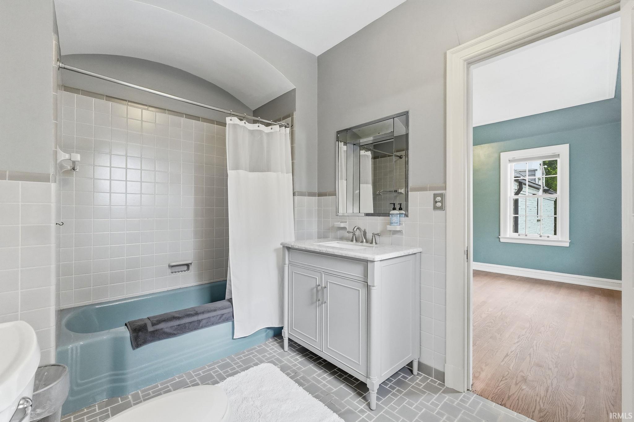 Bathroom with tiled walls, patterned floor tiles, a built-in bathtub, a vanity with a counter and sink, and a mirrored medicine cabinet