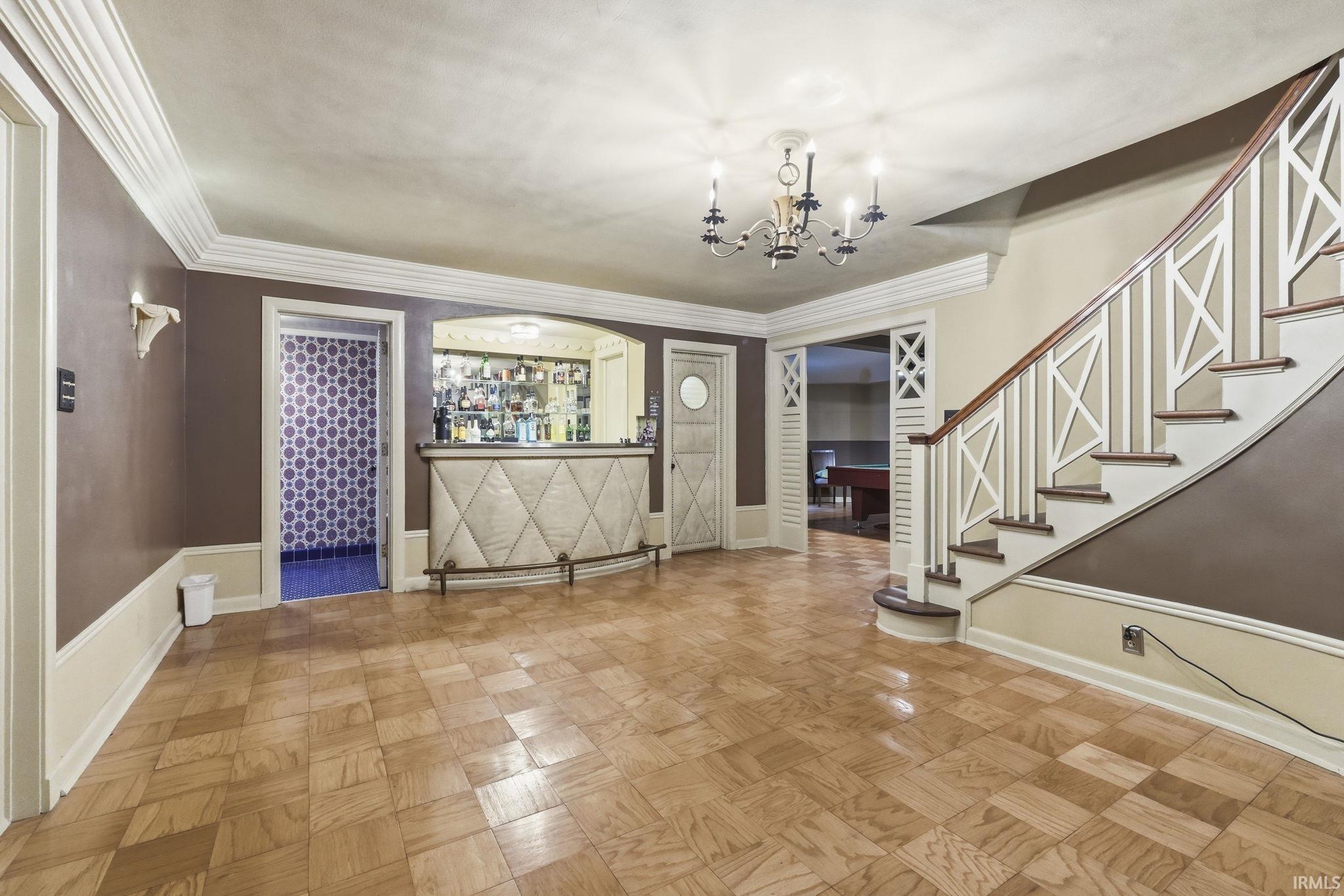 Elegant foyer showcasing herringbone wood-finish flooring, a curved staircase with decorative X-pattern railings, crown molding, and a chandelier