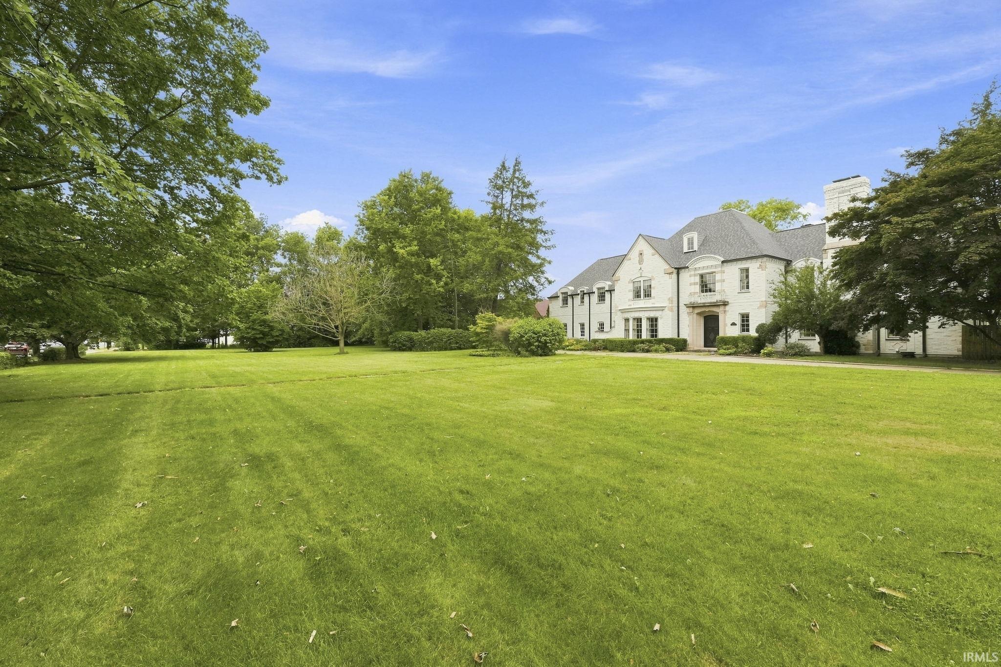 Expansive front lawn with mature trees and a grand white stucco exterior