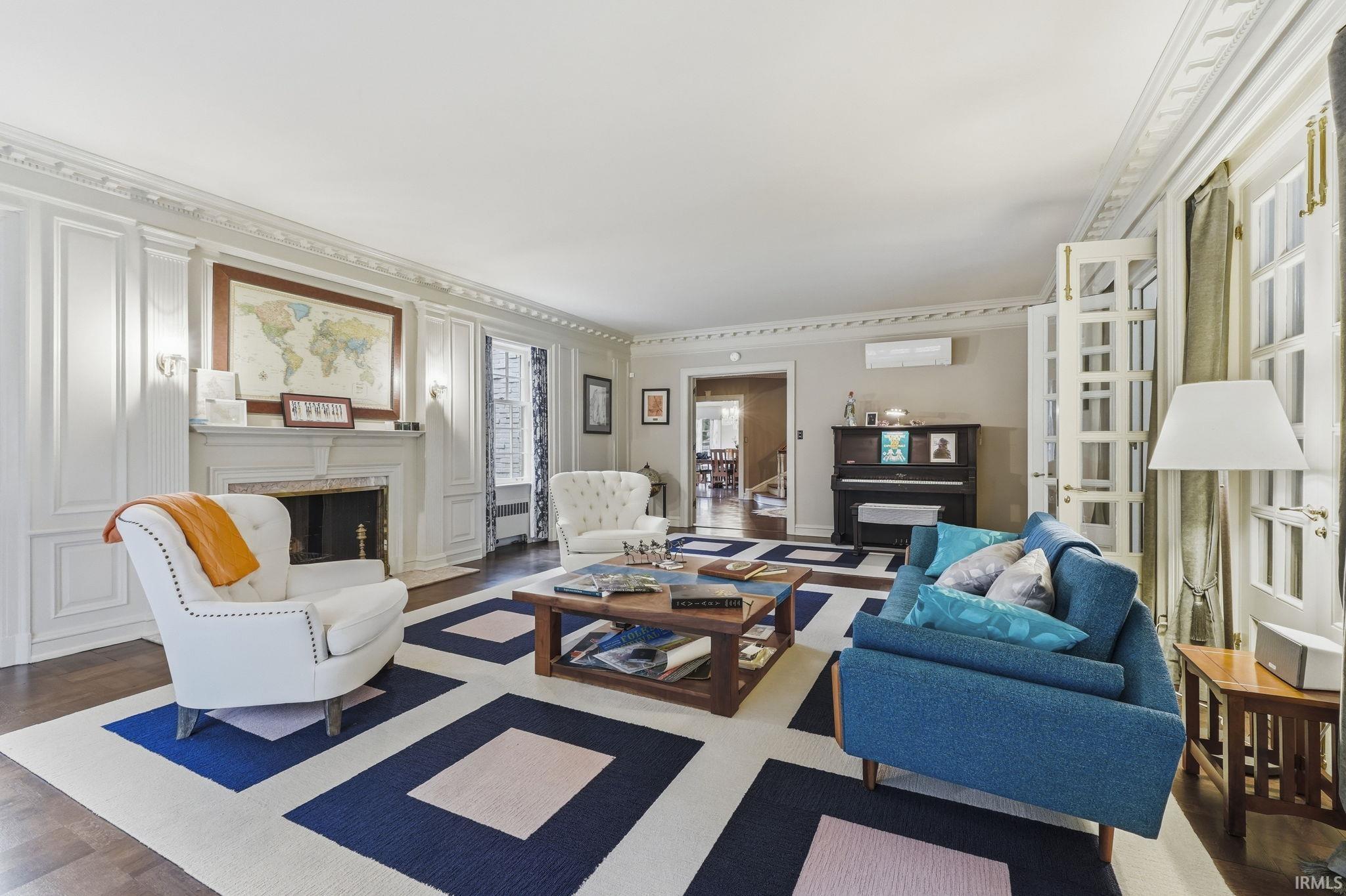 Elegant living room featuring hardwood flooring, a decorative fireplace with white surround and mantel, coffered ceiling with crown molding, and built-in cabinetry with glass-front doors