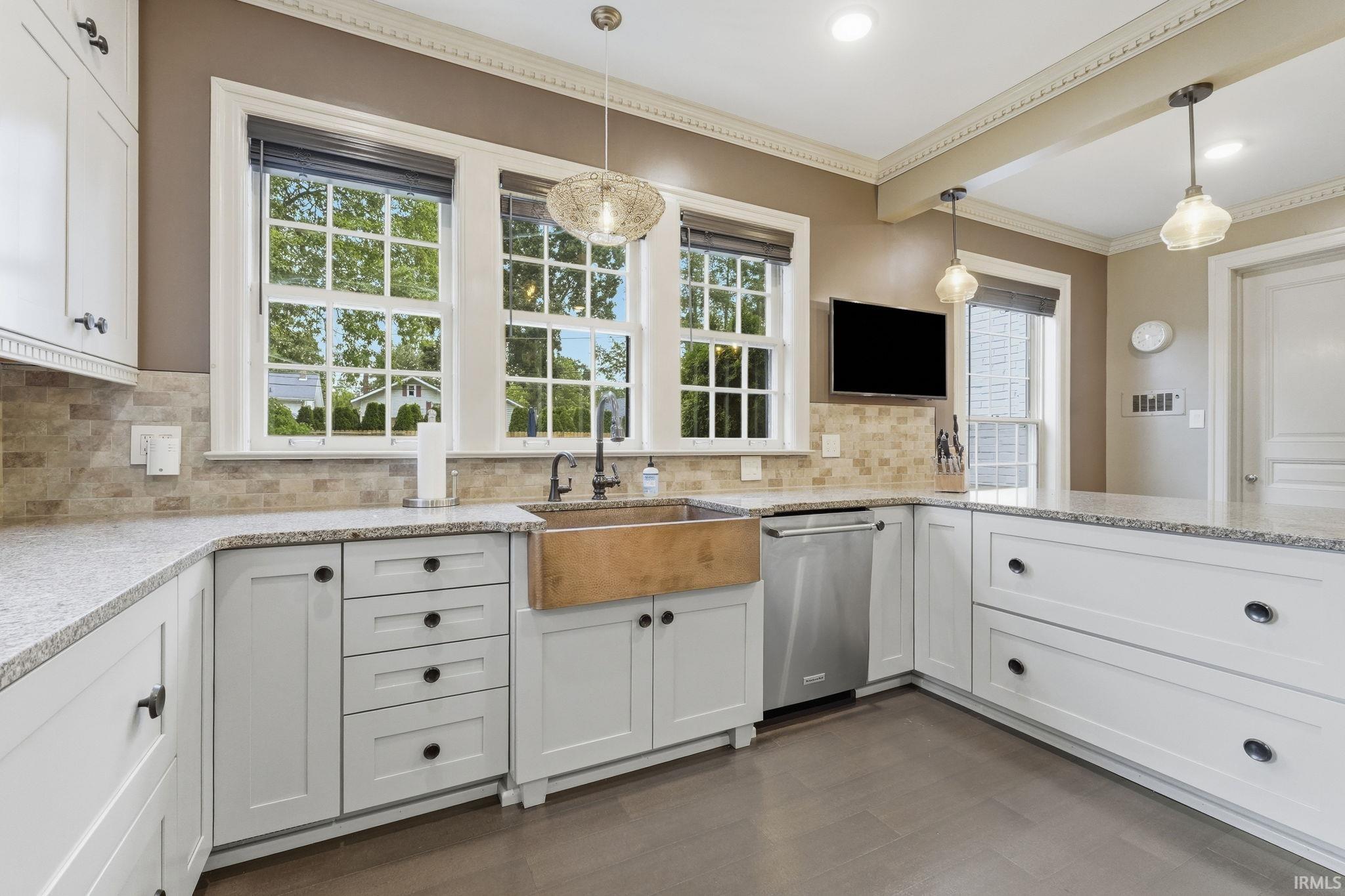 White shaker-style cabinetry with dark hardware, light speckled countertops, a wood-finish farmhouse sink, and stainless steel appliances