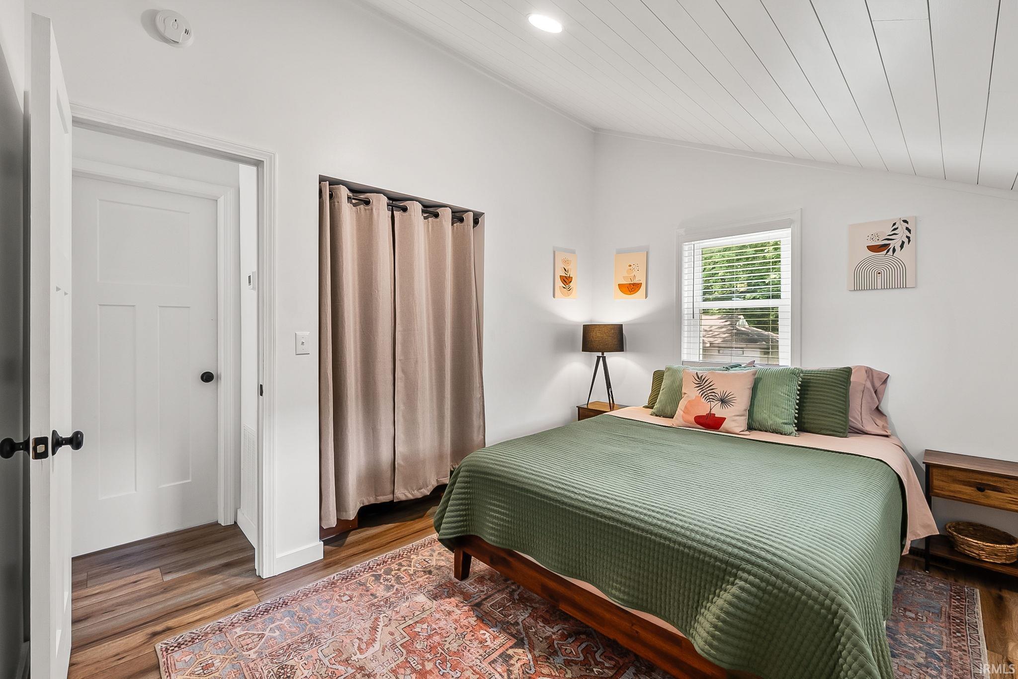 Vaulted ceiling with white wood paneling, wood-finish flooring, white walls, and a window with blinds