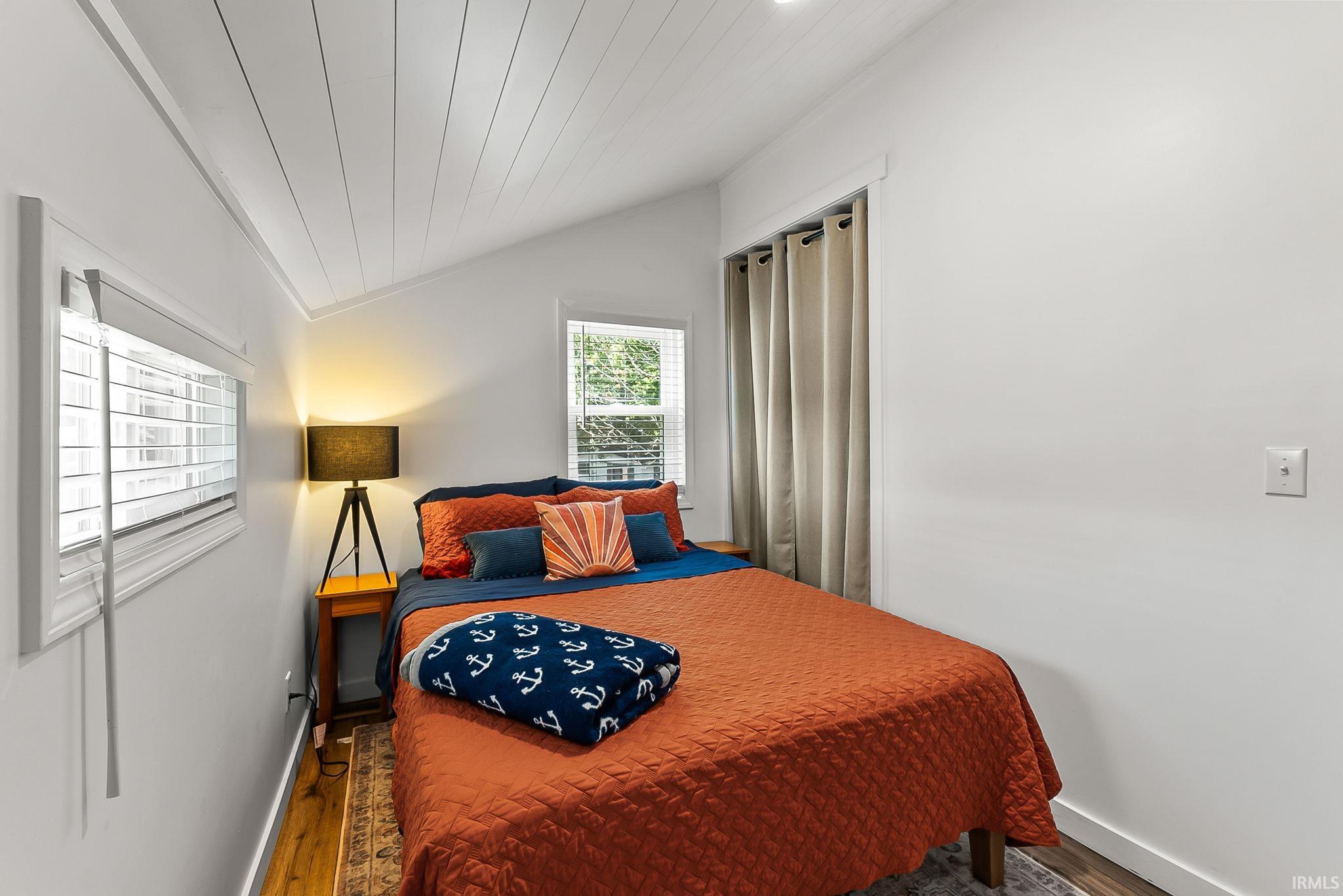 Bright secondary bedroom featuring hardwood flooring, vaulted plank ceiling, and abundant natural light from dual windows