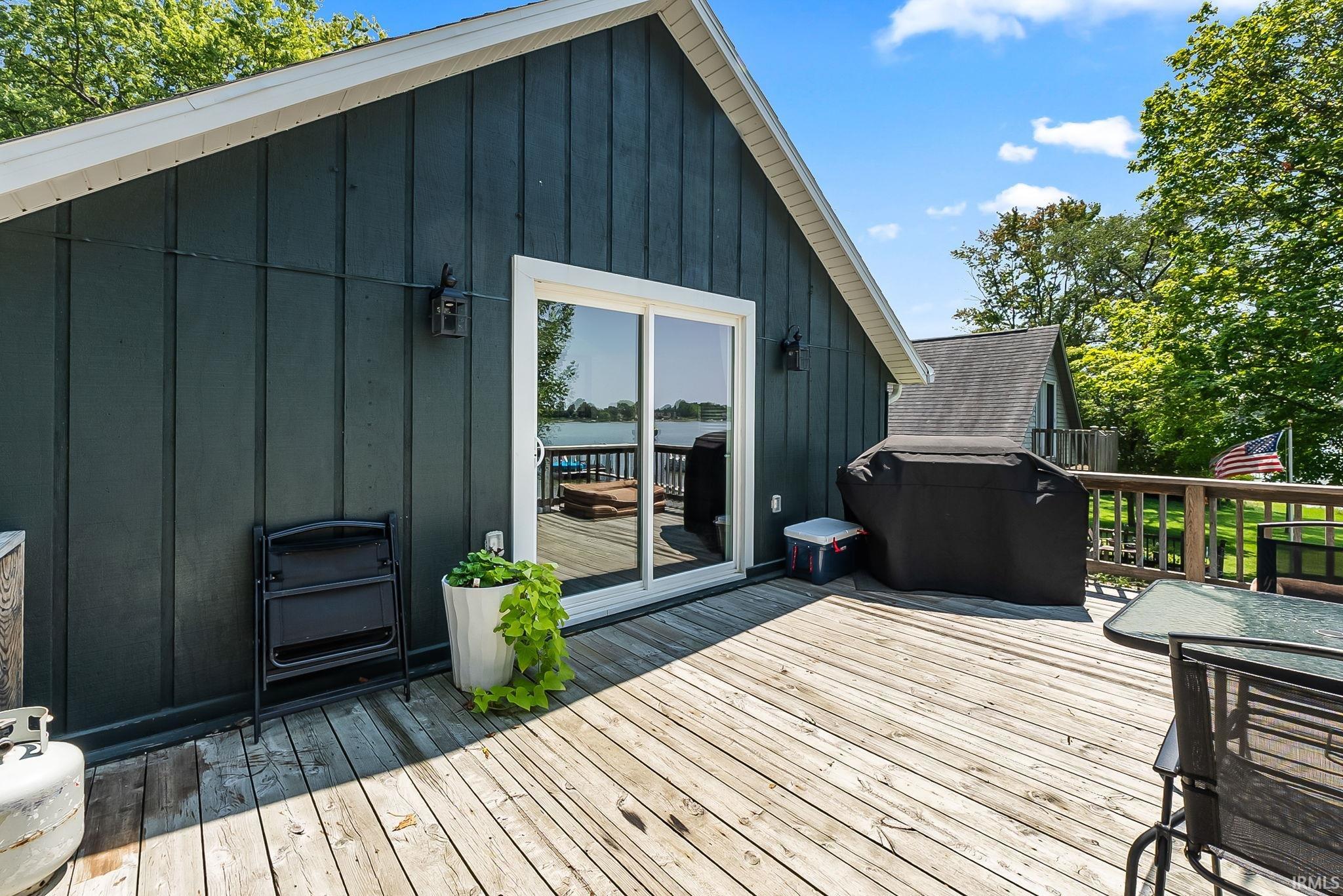 Expansive outdoor deck with wood flooring and dark wood paneling, featuring a sliding glass door and a railing