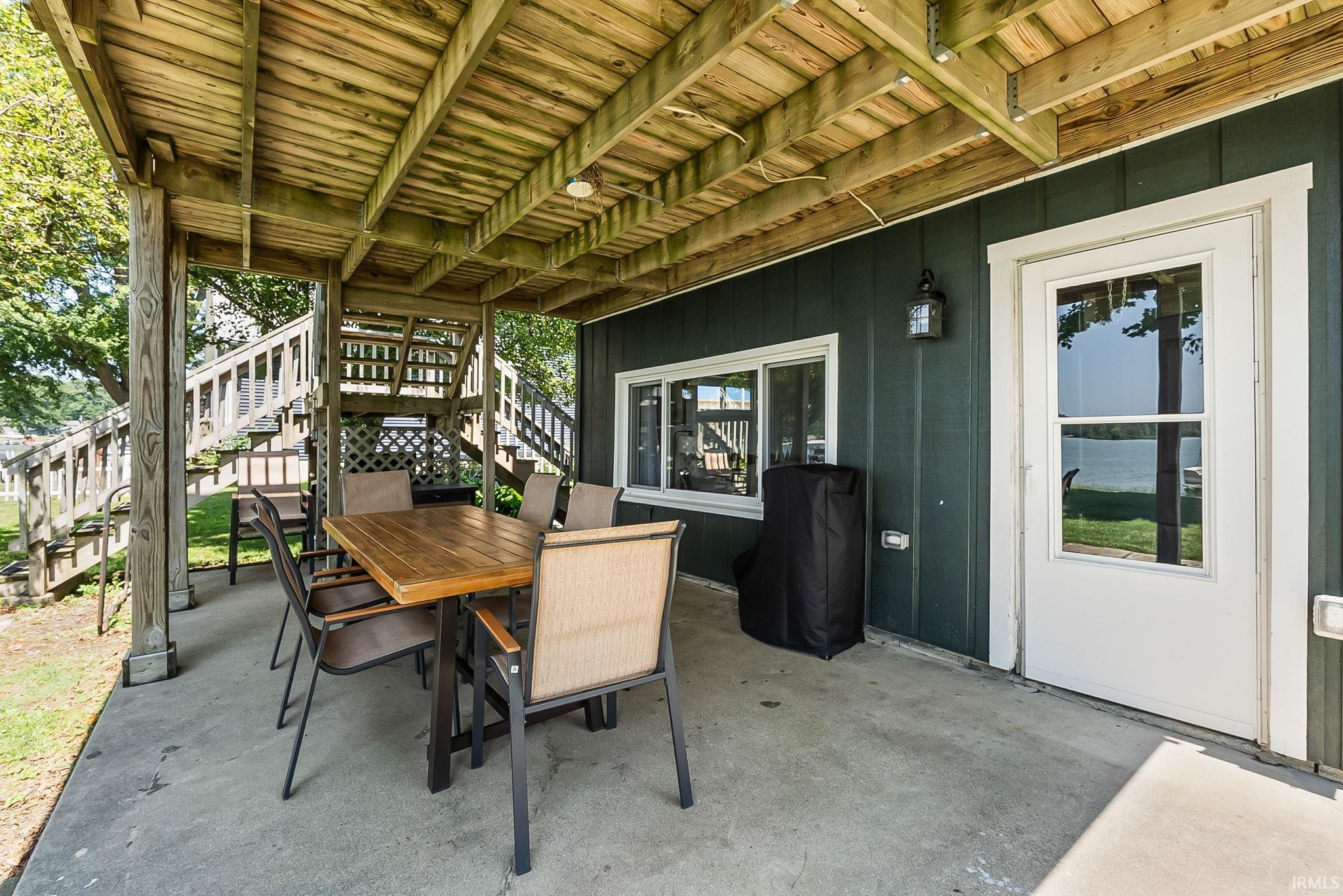Underdeck patio with wood plank ceiling, concrete flooring, exterior siding, and a glass-paneled door