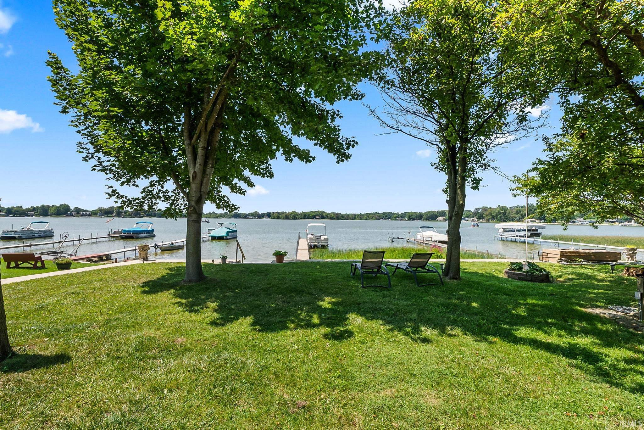 Expansive green lawn with mature trees, offering waterfront access with multiple docks and clear water