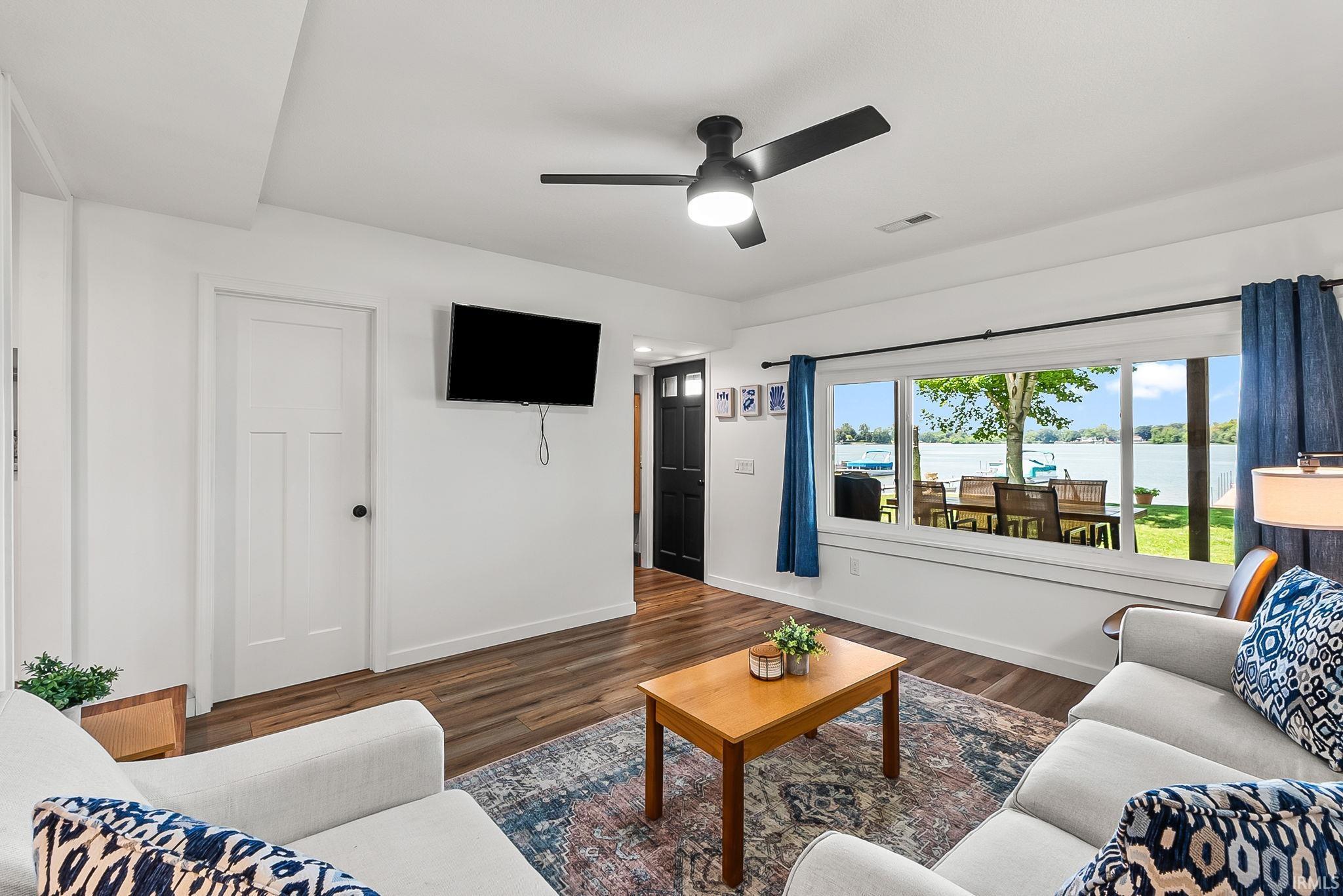 Bright living area showcasing wood-finish flooring, a ceiling fan with integrated lighting, and a wall-mounted flat-screen television