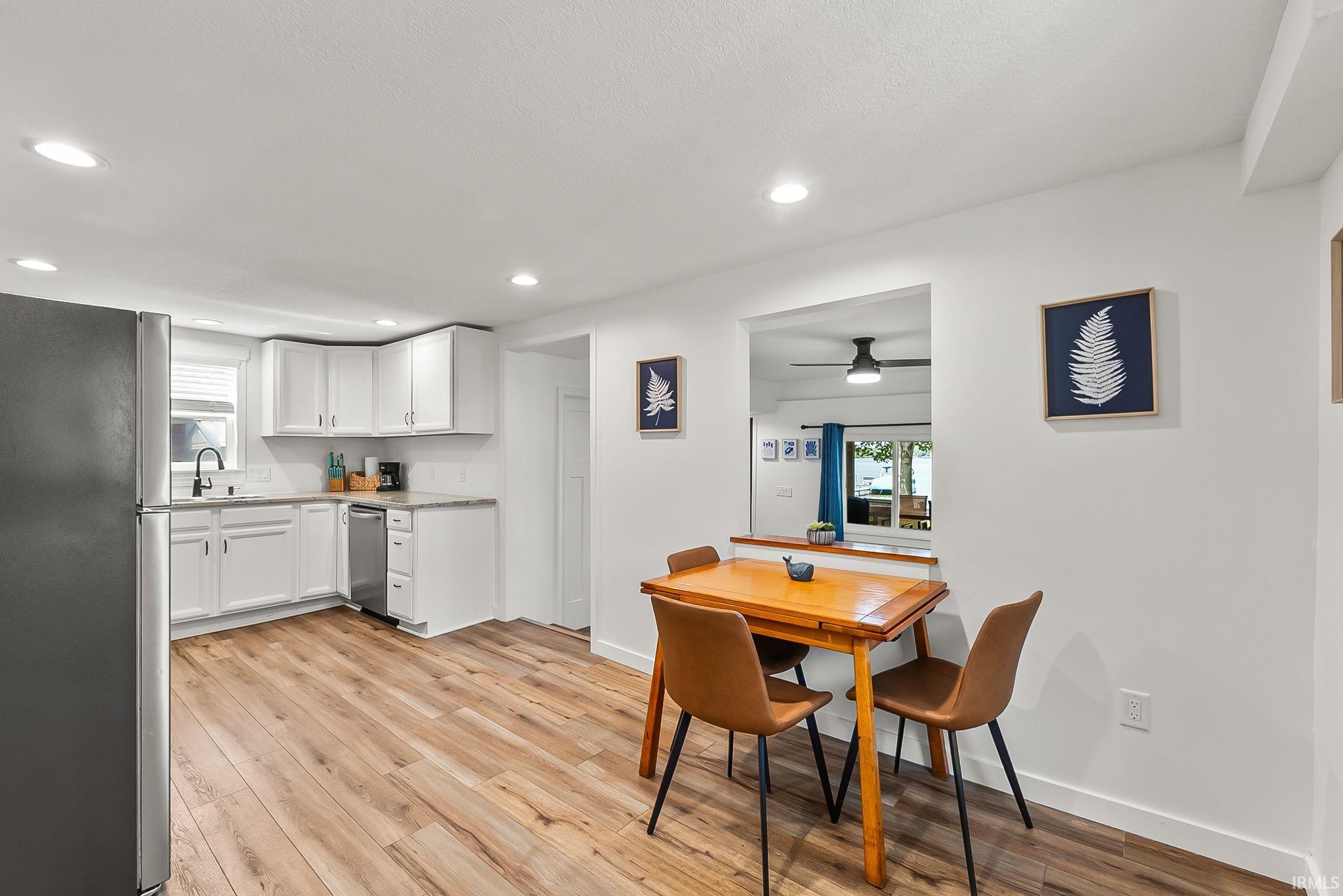 Open-concept kitchen and dining area featuring white cabinetry with stainless steel appliances, wood-finish flooring throughout, recessed ceiling lighting, and a wood dining table with seating for four