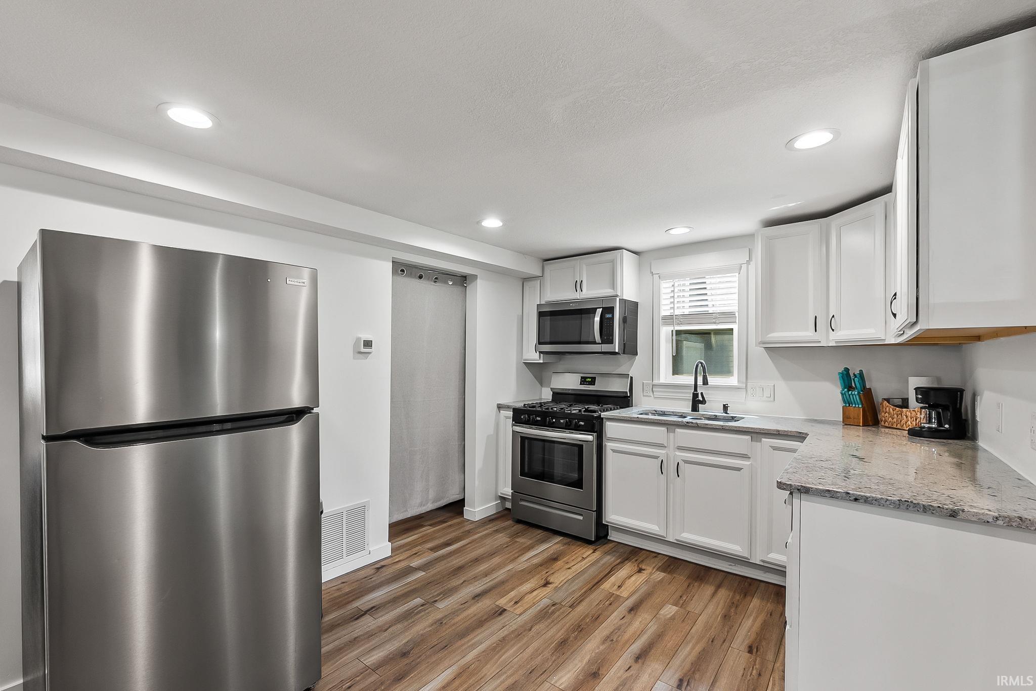 Modern kitchen featuring stainless steel appliances, white cabinetry with wood-finish countertop accents, granite-style countersurfaces, and wood-finish flooring throughout