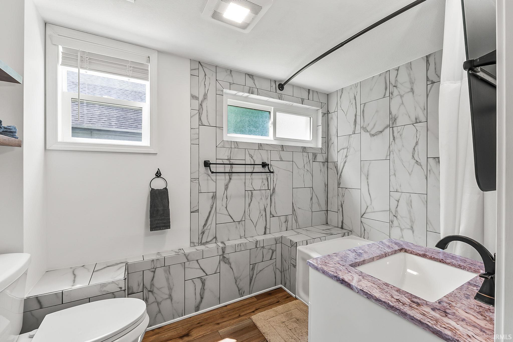 Bathroom featuring a vanity with an integrated sink and purple veined countertop, wood-finish flooring, and white and gray patterned wall tiling