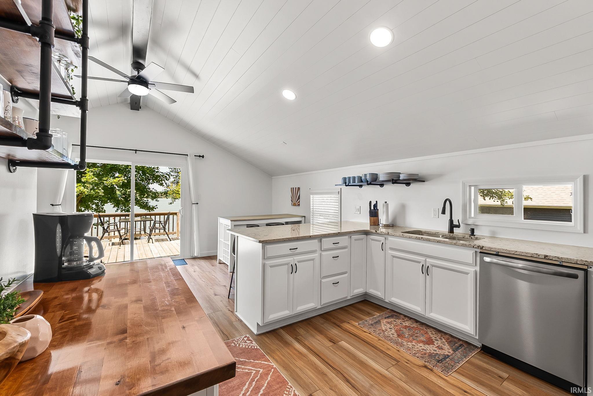 Kitchen with white cabinetry, granite countertops, stainless steel dishwasher, wood-finish flooring, and a vaulted ceiling