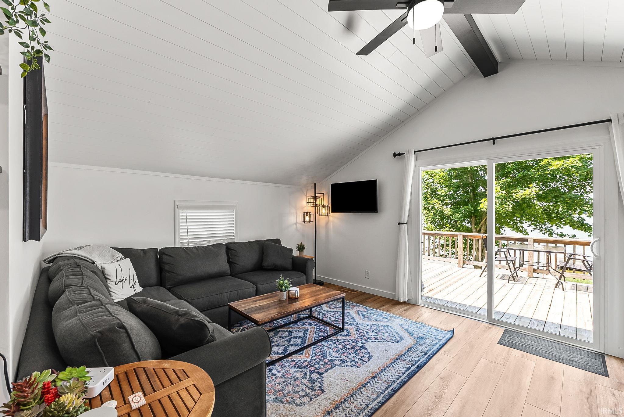 Vaulted ceiling featuring a ceiling fan, wood-finish flooring, and sliding glass doors opening to a wood deck with a wood railing
