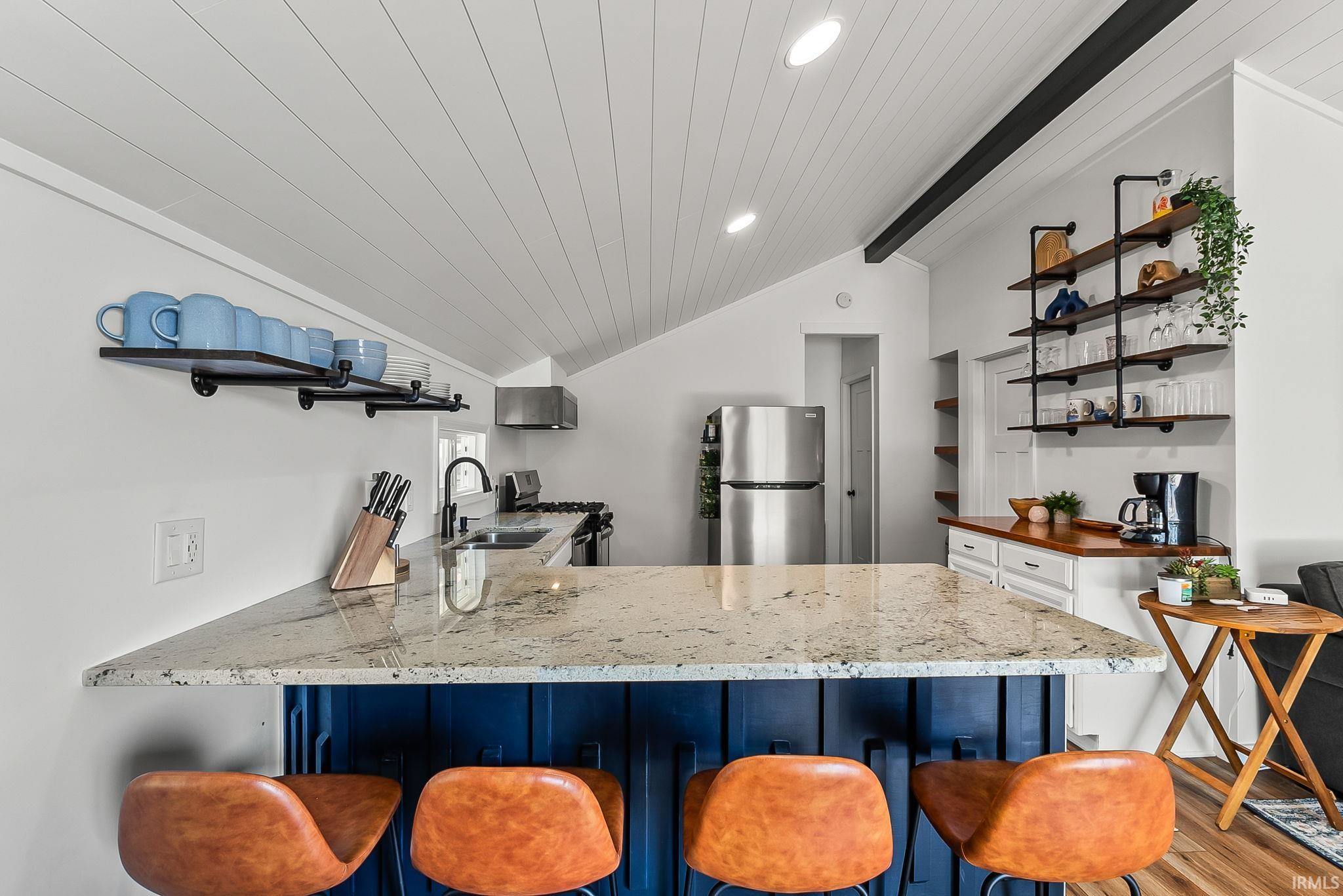 Kitchen featuring a vaulted ceiling with paneling, a stone-finish countertop, dark blue cabinetry, and stainless steel appliances
