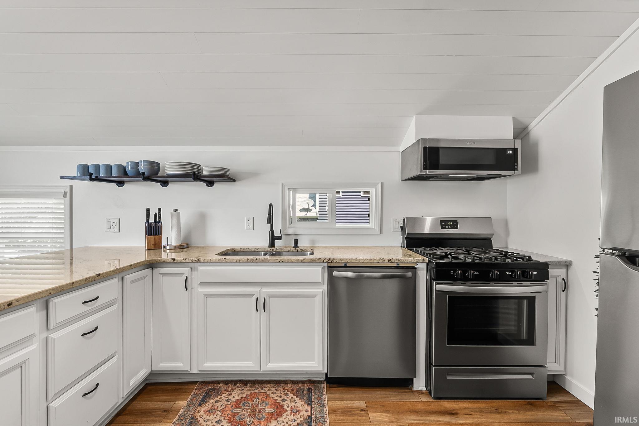 Updated kitchen featuring white cabinetry with brushed nickel hardware, wood-finish countertops, stainless steel appliances including a gas range and built-in microwave, and wood-finish flooring throughout the space