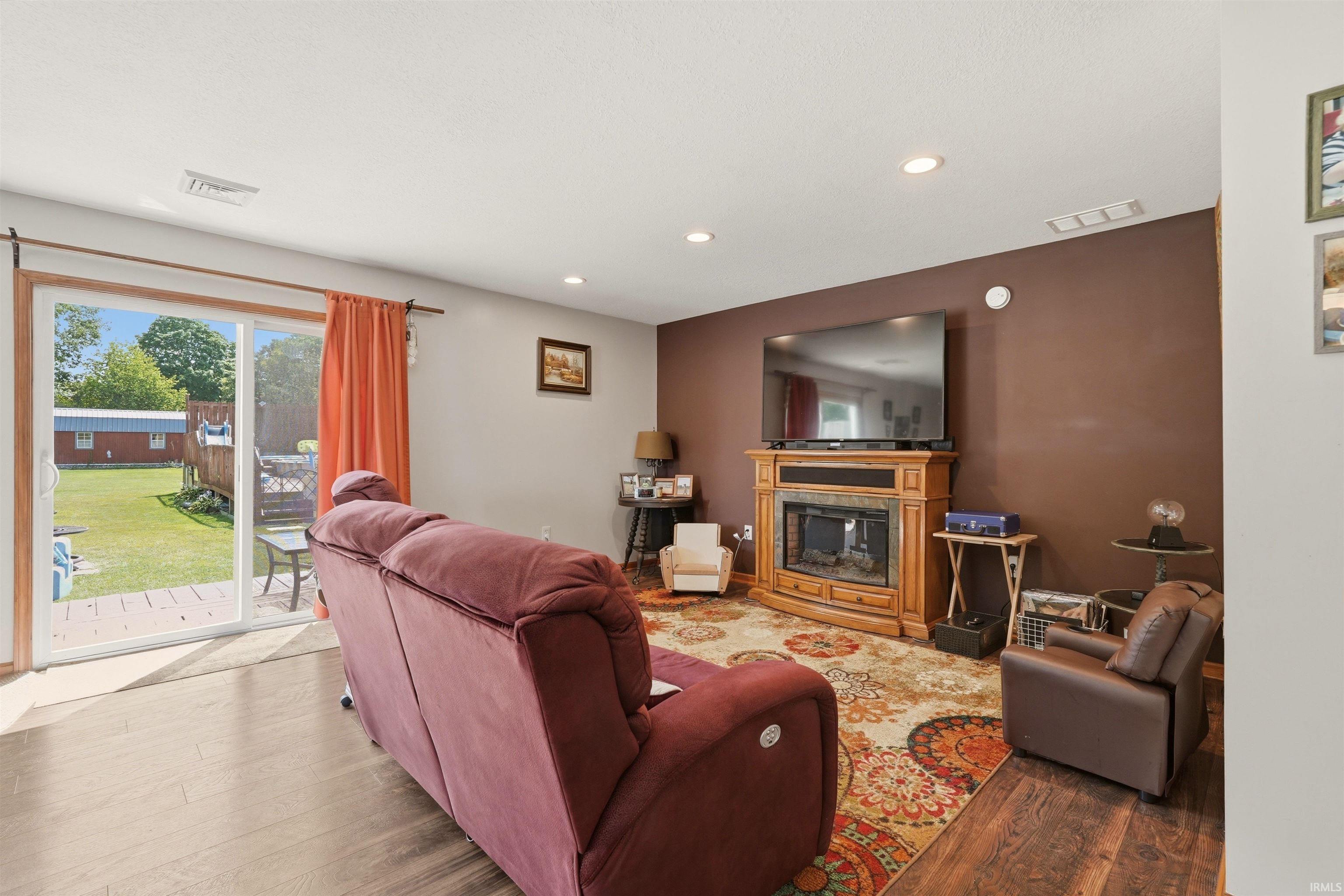 Wood-finish flooring throughout, recessed ceiling lighting, a built-in fireplace with a wood surround, and sliding glass doors to the exterior