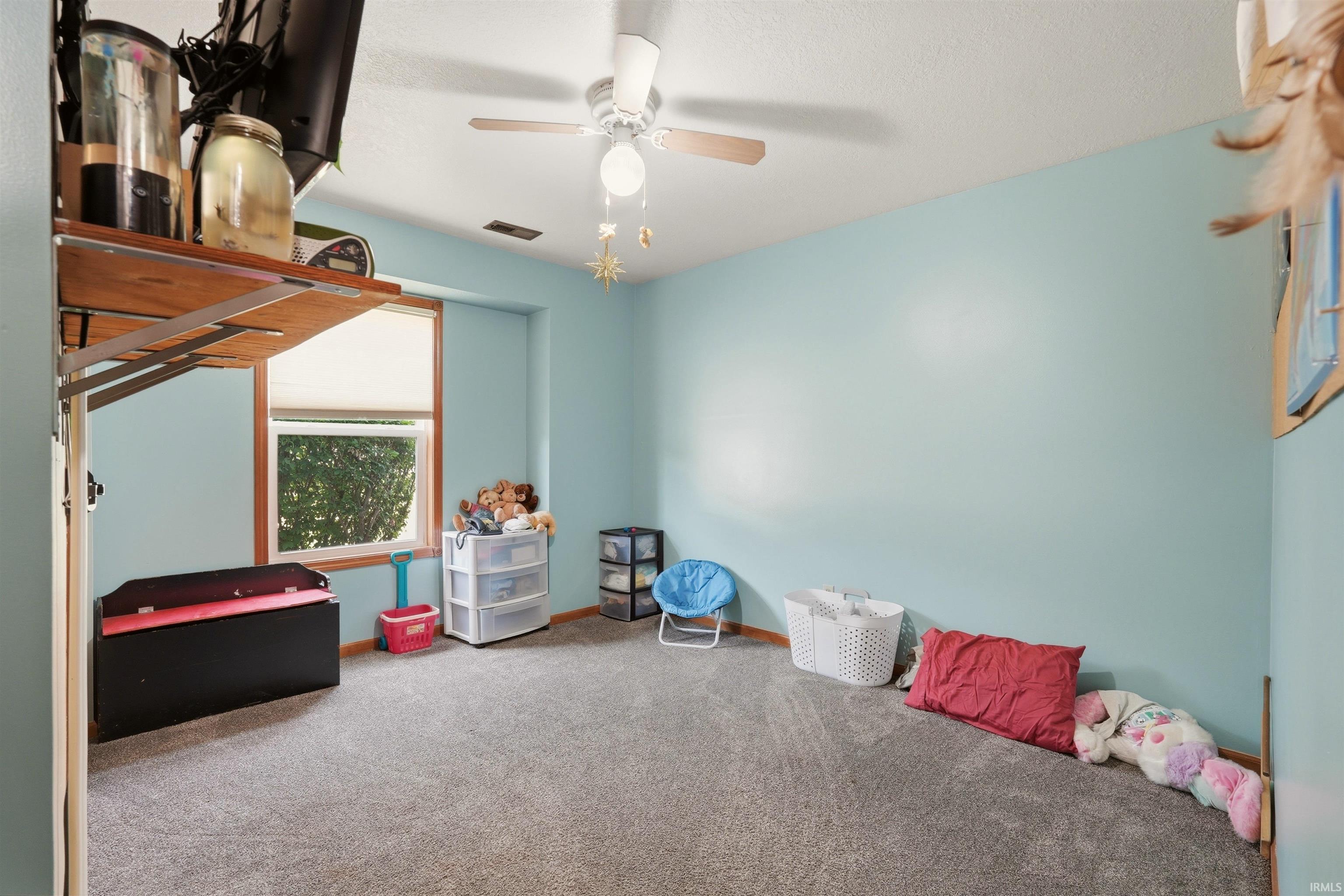 Carpeted room featuring a ceiling fan, a window with wood trim, and a built-in wall shelf