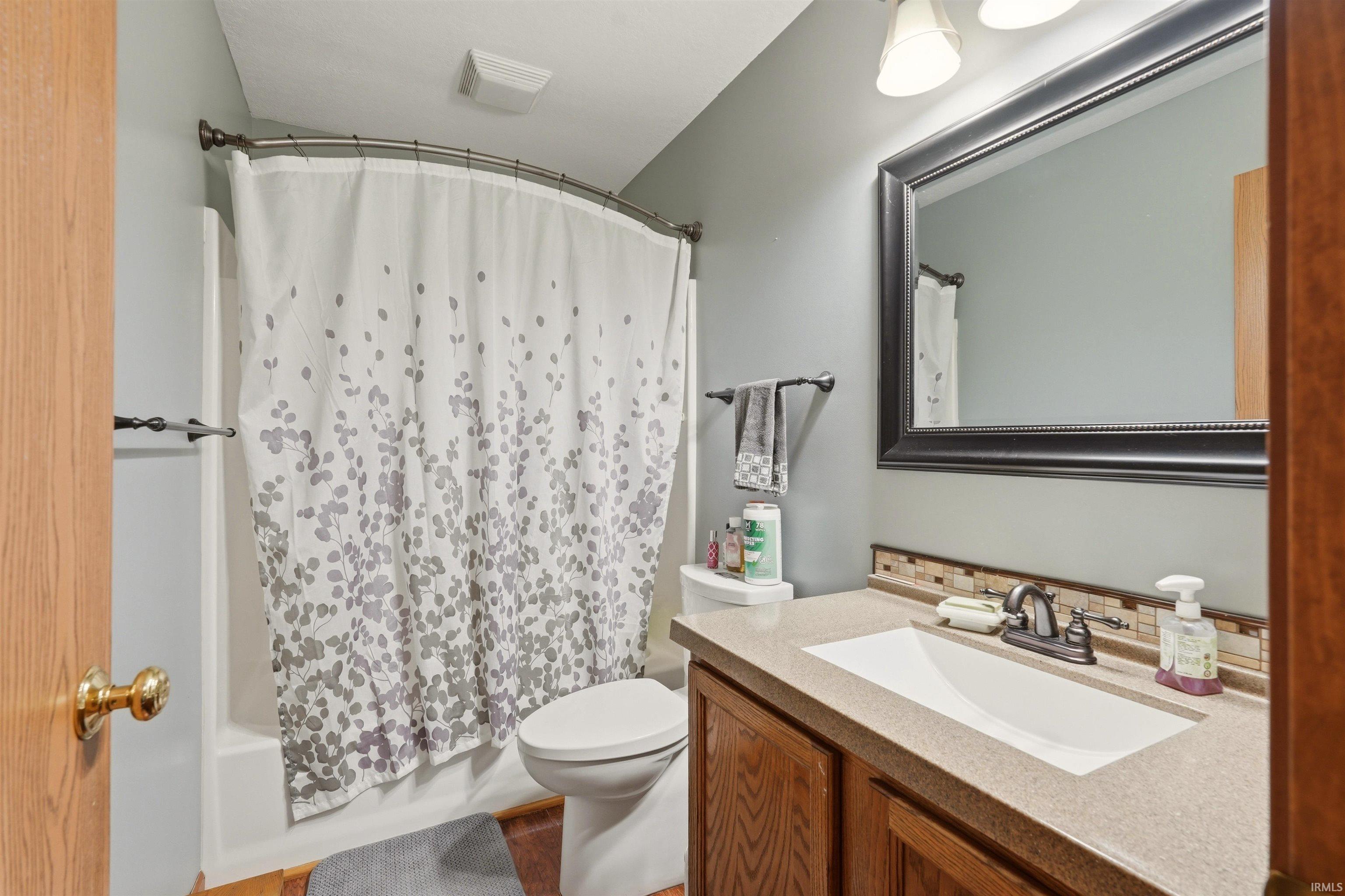 Bathroom featuring a single vanity with wood cabinetry, a tiled backsplash, a framed mirror, and a shower-tub combination