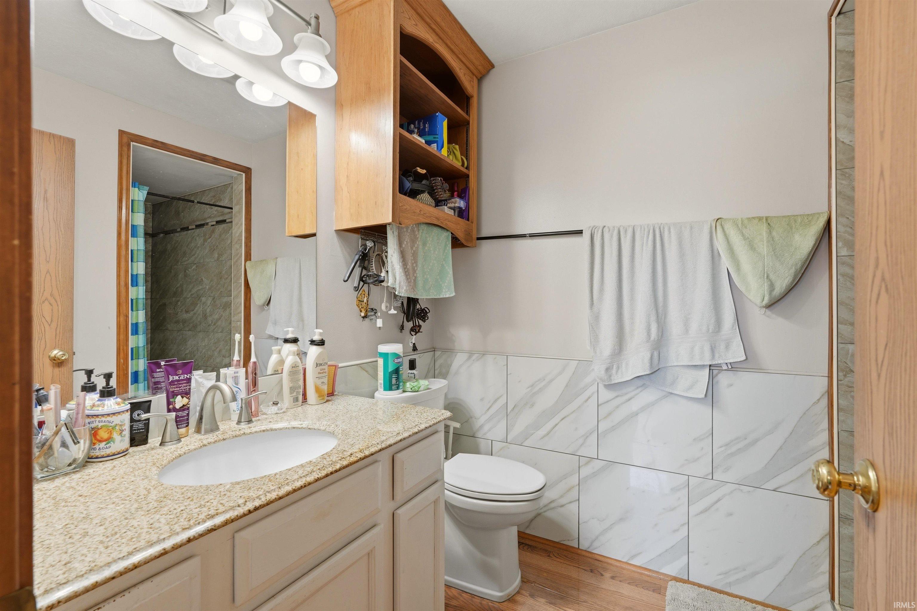 Wood-finish flooring with a white vanity featuring a granite countertop and an undermount sink