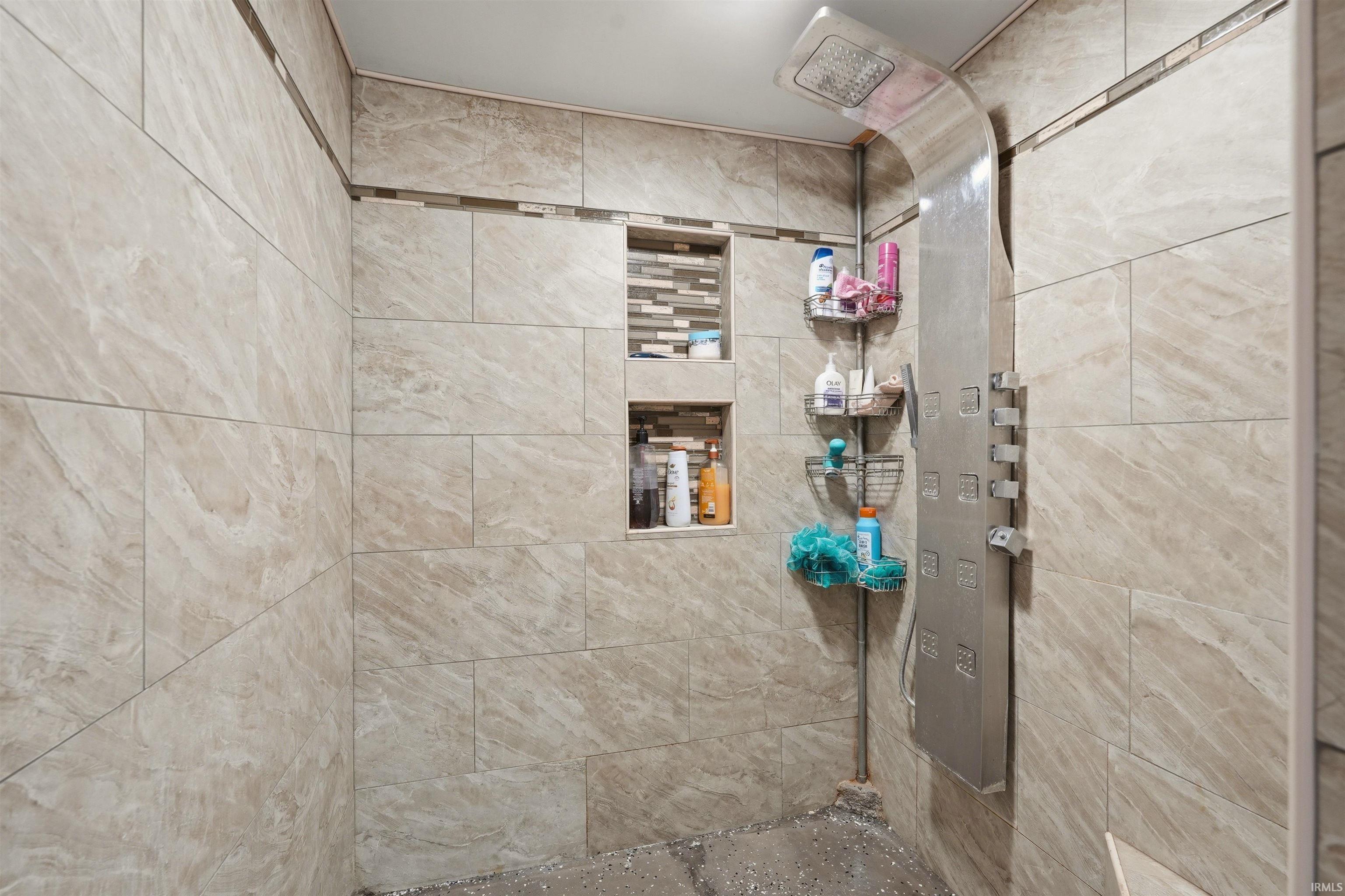 Tiled shower with a rainfall shower head, multiple body sprays, and dual recessed shelves