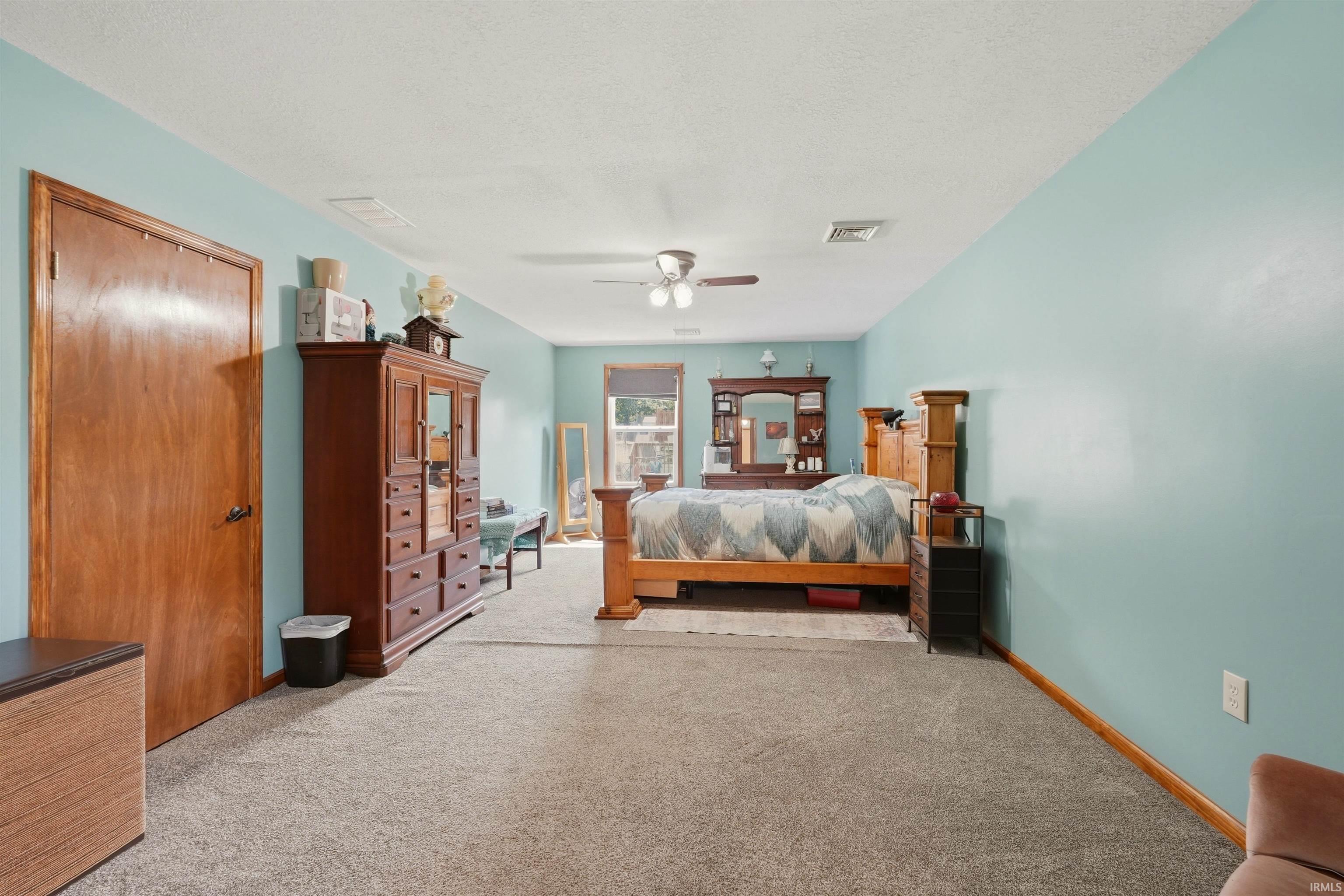 Light-colored carpeting with contrasting baseboards, a wood-finish door, and a ceiling fan with integrated lighting