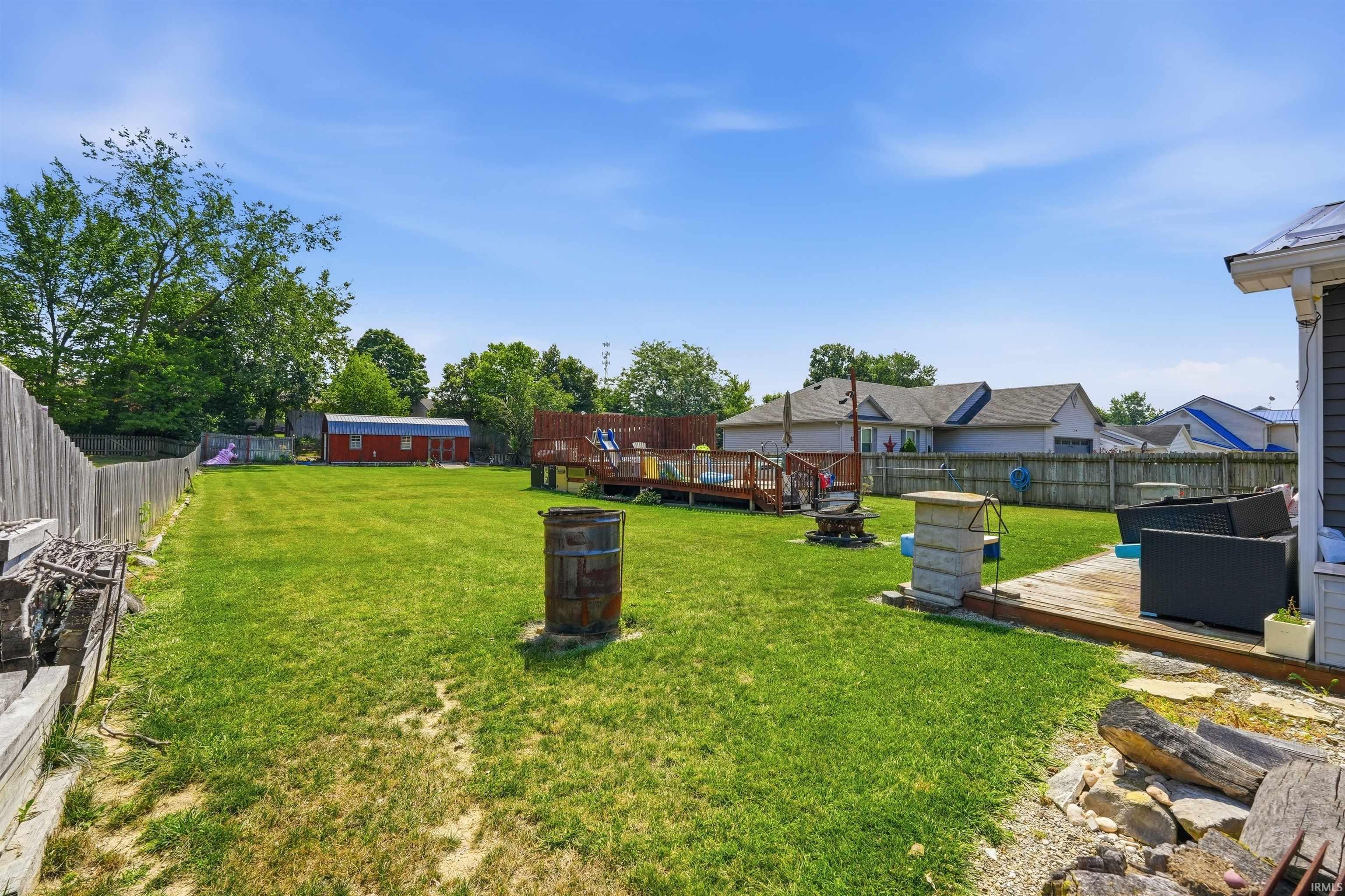 Expansive backyard featuring a wood privacy fence, a multi-level wood deck, and a red shed with a metal roof