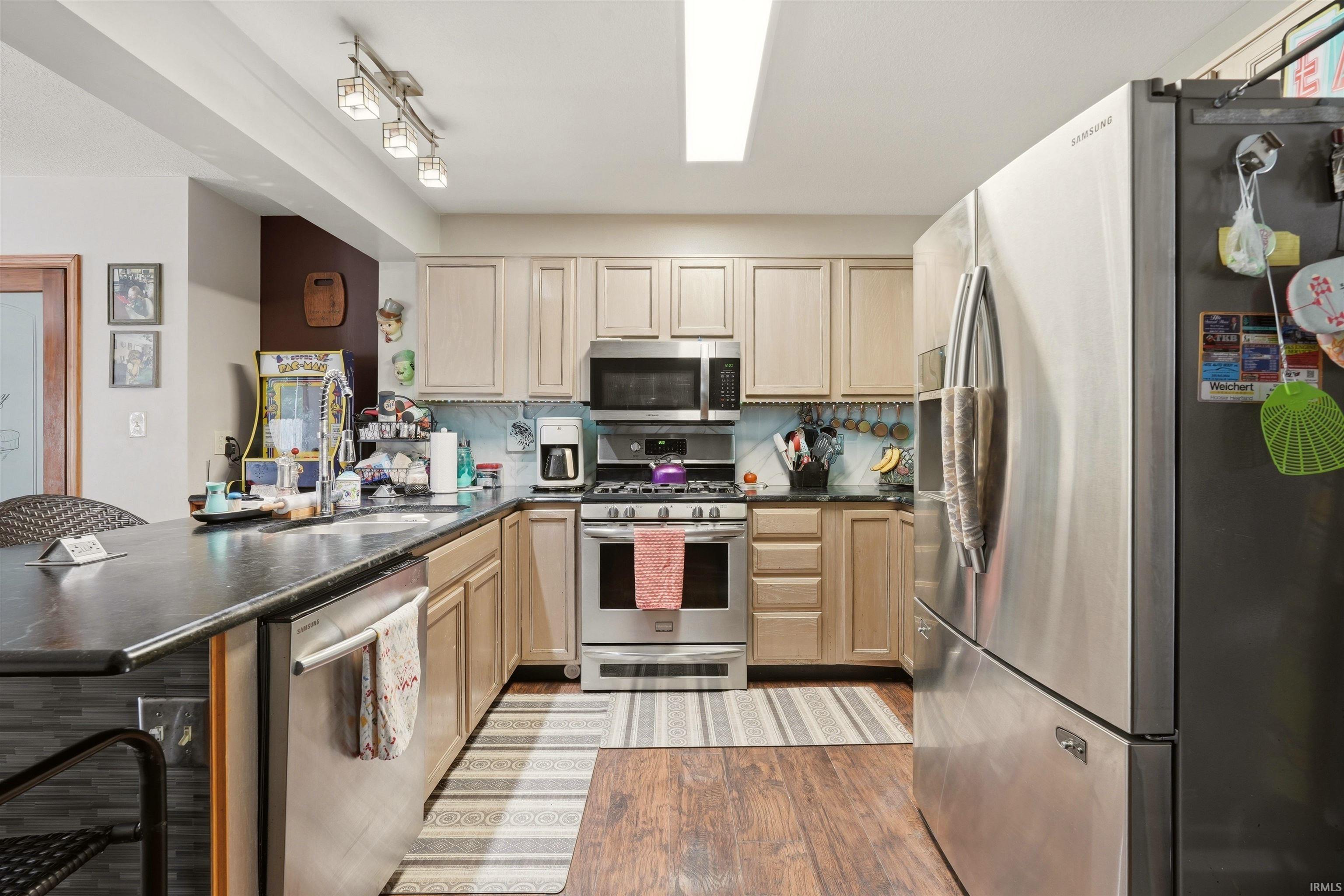 Kitchen featuring stainless steel appliances, wood-finish flooring, a built-in dishwasher, light-toned cabinetry, and dark countertops