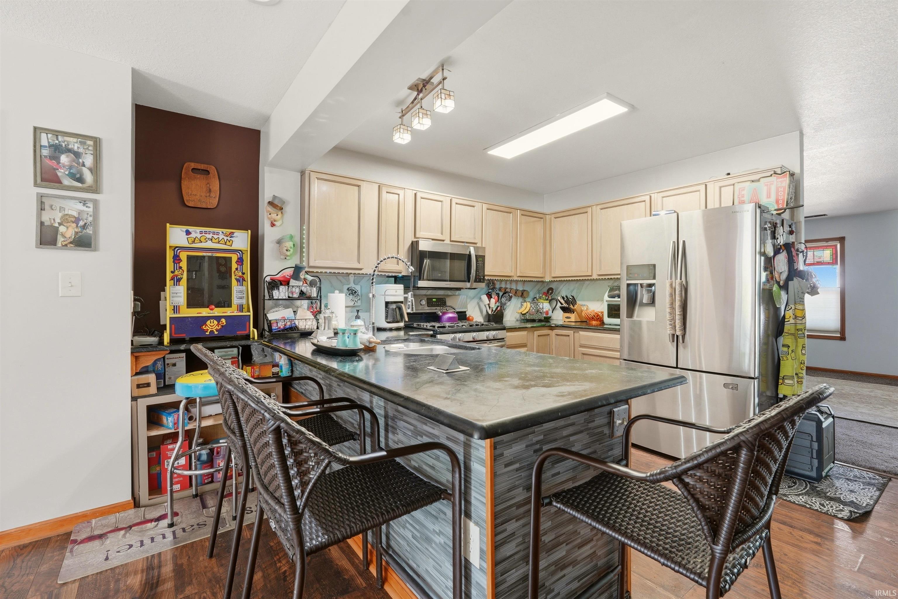 Kitchen featuring wood-finish flooring, light wood cabinetry, stainless steel appliances, a tiled backsplash, and a large island with a tiled base