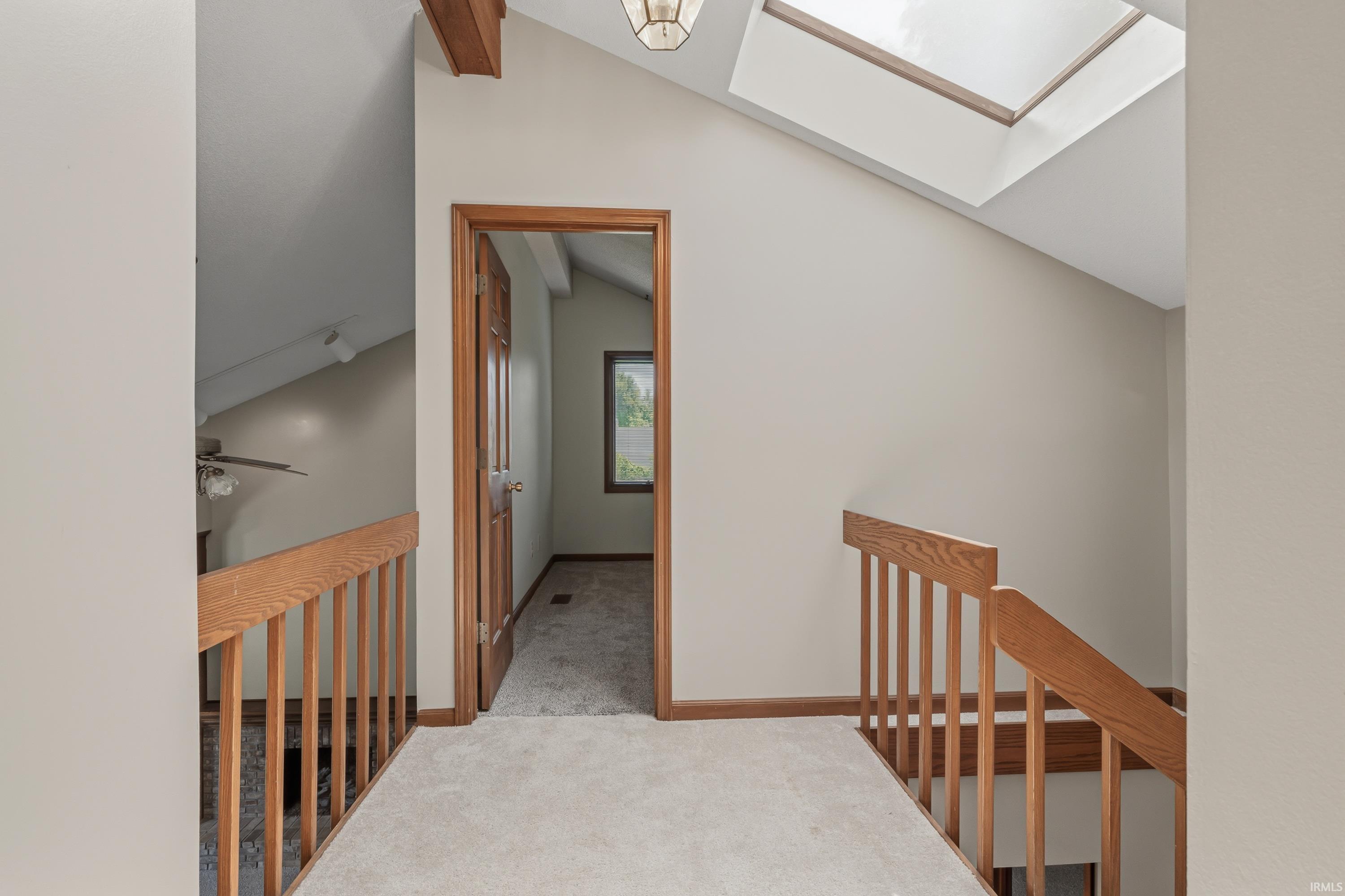 Carpeted hallway with wood railing and trim, wood-beamed ceiling, and skylight