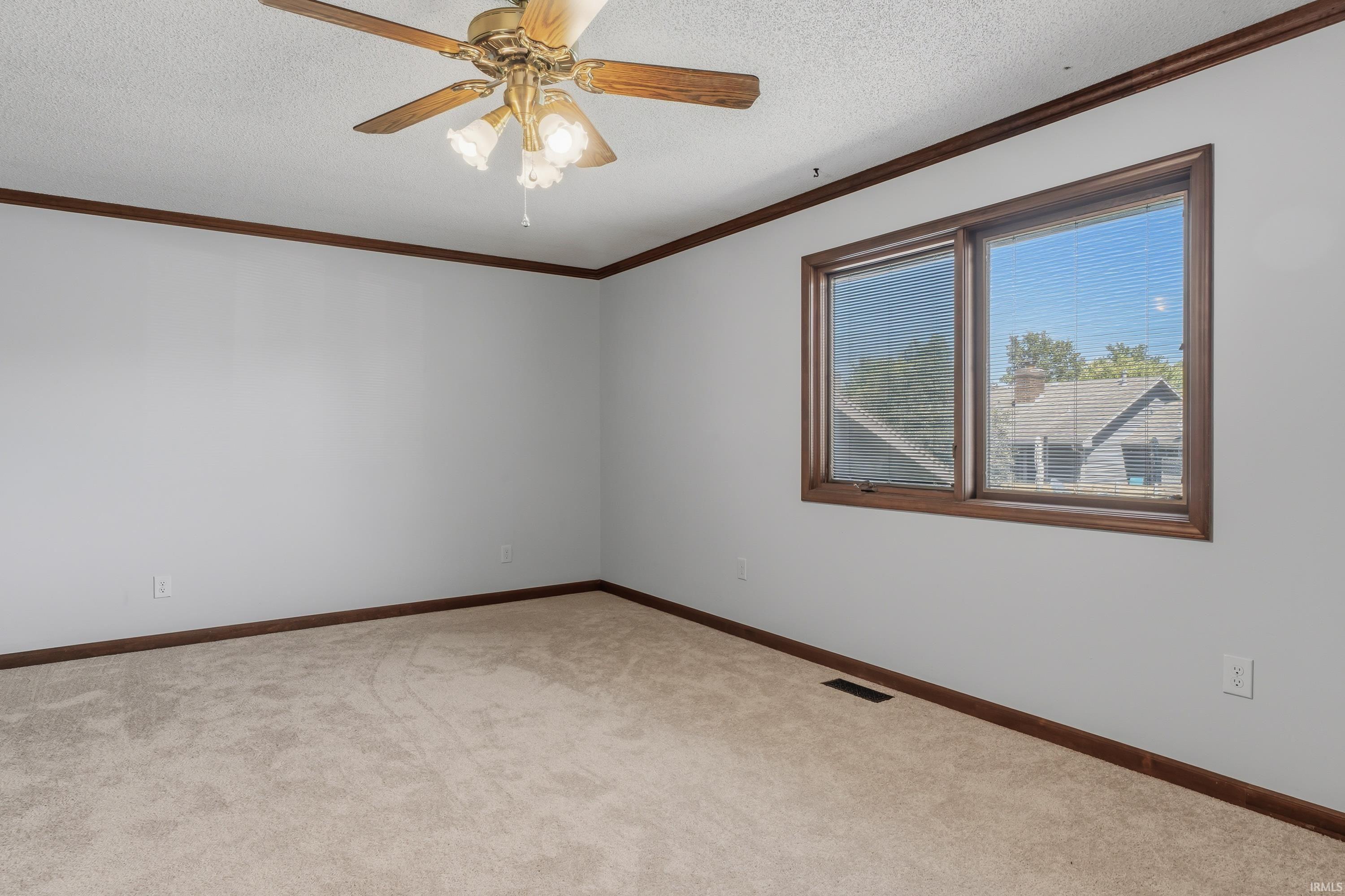 Neutral-toned carpeting, ceiling fan with integrated lighting, wood-trimmed windows, and wood crown molding