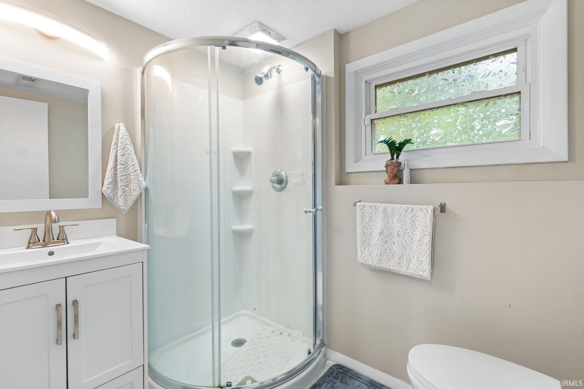 Curved glass shower enclosure, white vanity with integrated sink, brushed nickel faucet, framed mirror, and a frosted glass window