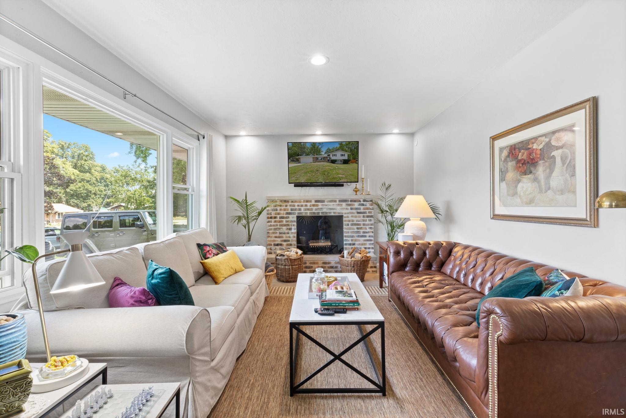 Expansive windows providing natural light, brick-clad fireplace, wood-finish flooring, recessed lighting, and crown molding
