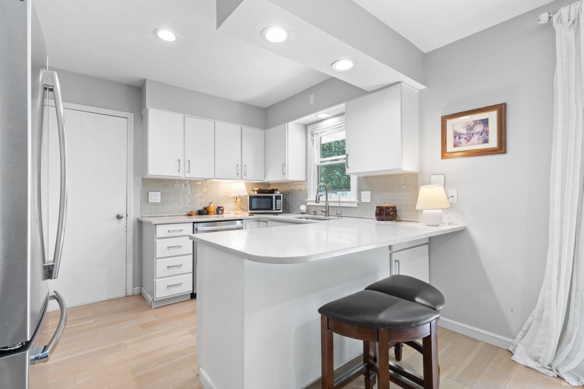 Contemporary kitchen featuring white cabinetry, light-toned wood-finish flooring, recessed lighting, a stone countertop, and a tile backsplash