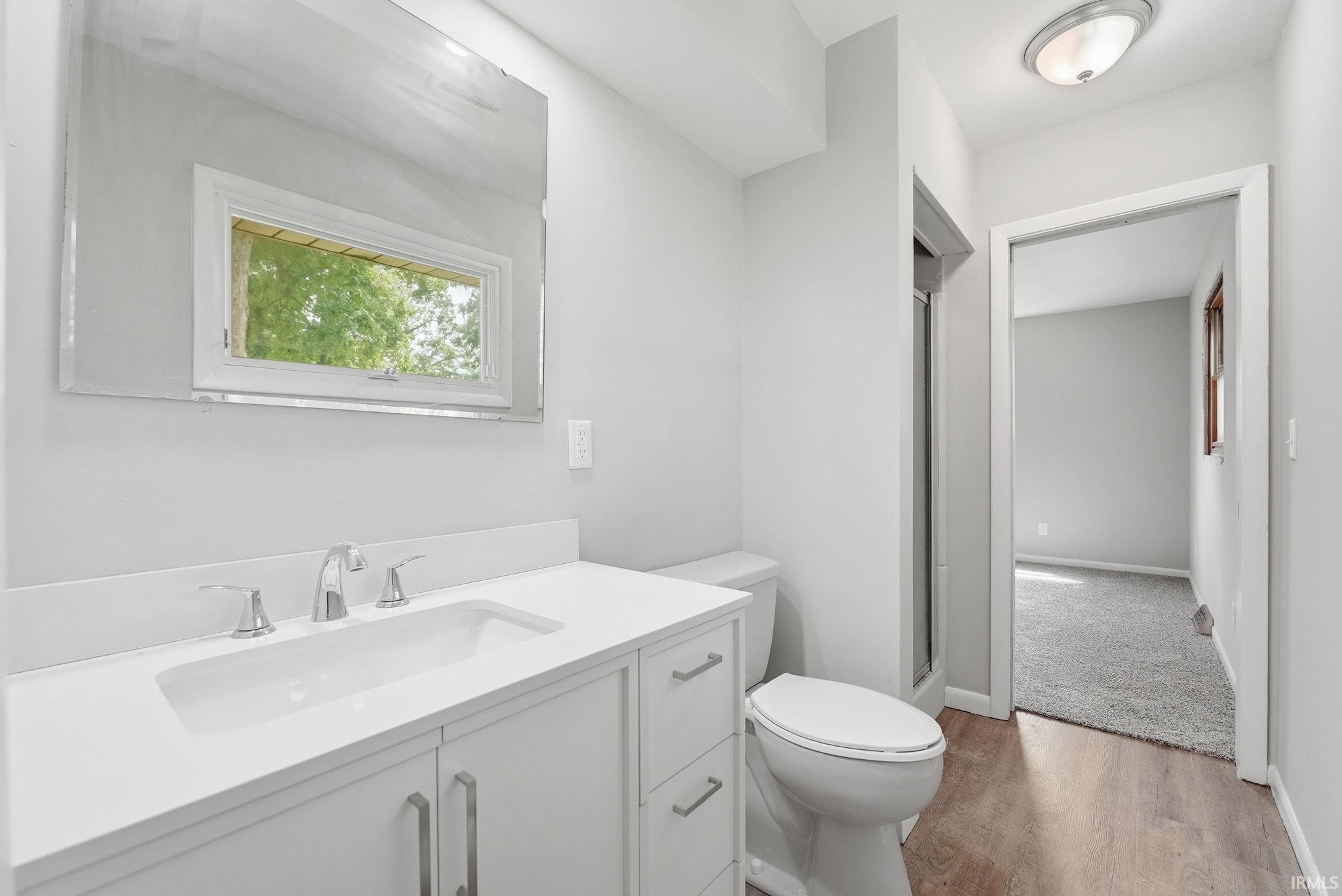 Bathroom featuring a white vanity with an integrated sink, polished chrome faucet, wood-finish flooring, and a window