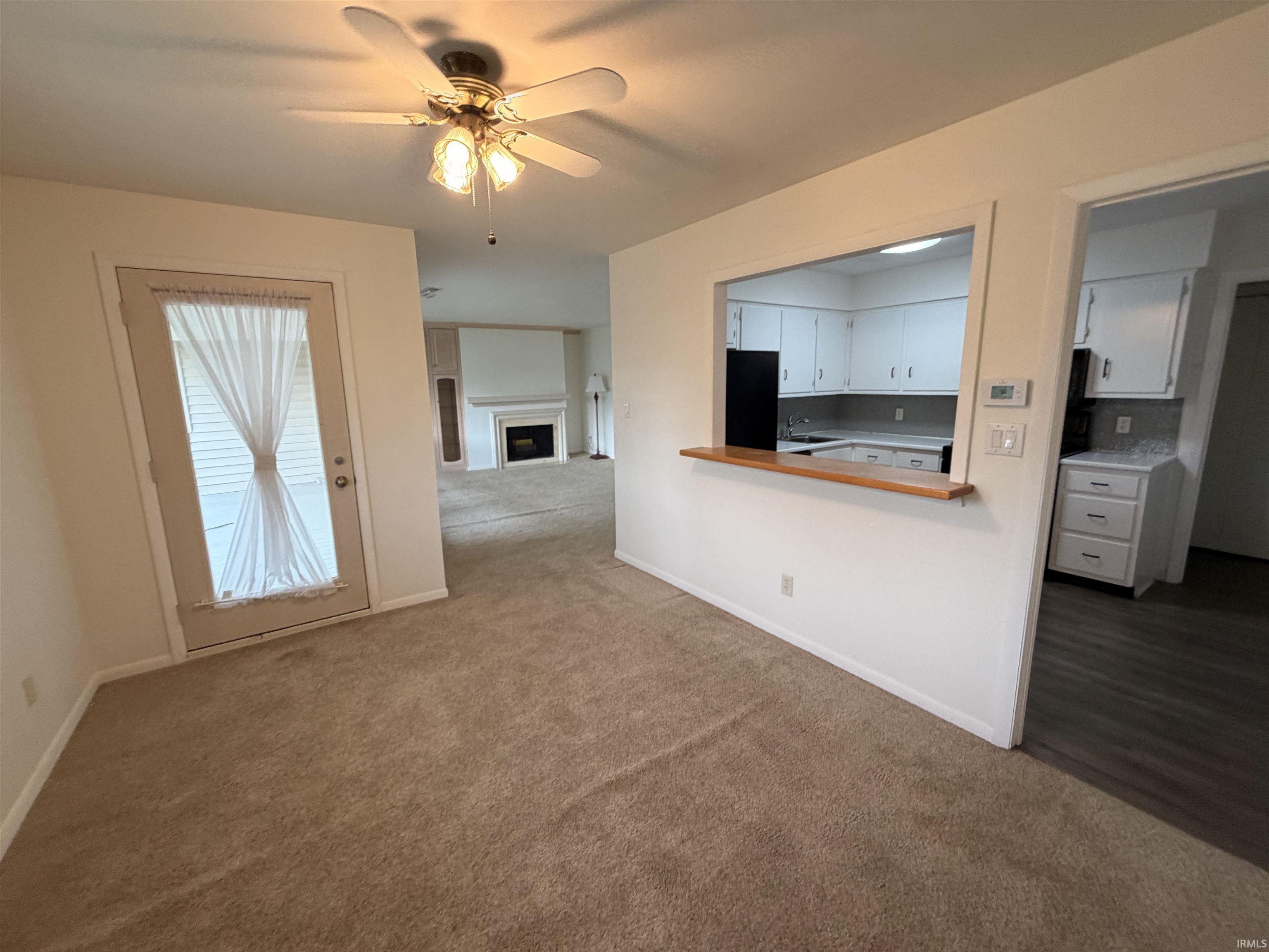 Neutral-toned carpet flooring, white walls, ceiling fan, pass-through window with wood ledge, and a full-light door