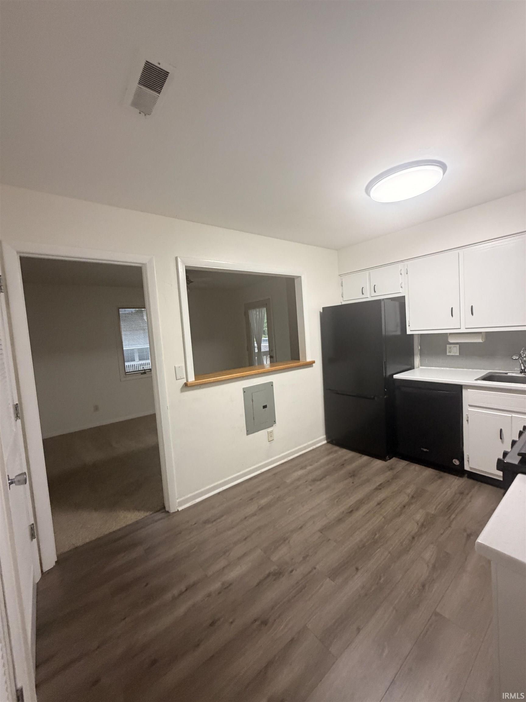 Kitchen featuring wood-finish flooring, white cabinetry, black appliances, a pass-through window, and a flush-mount ceiling light