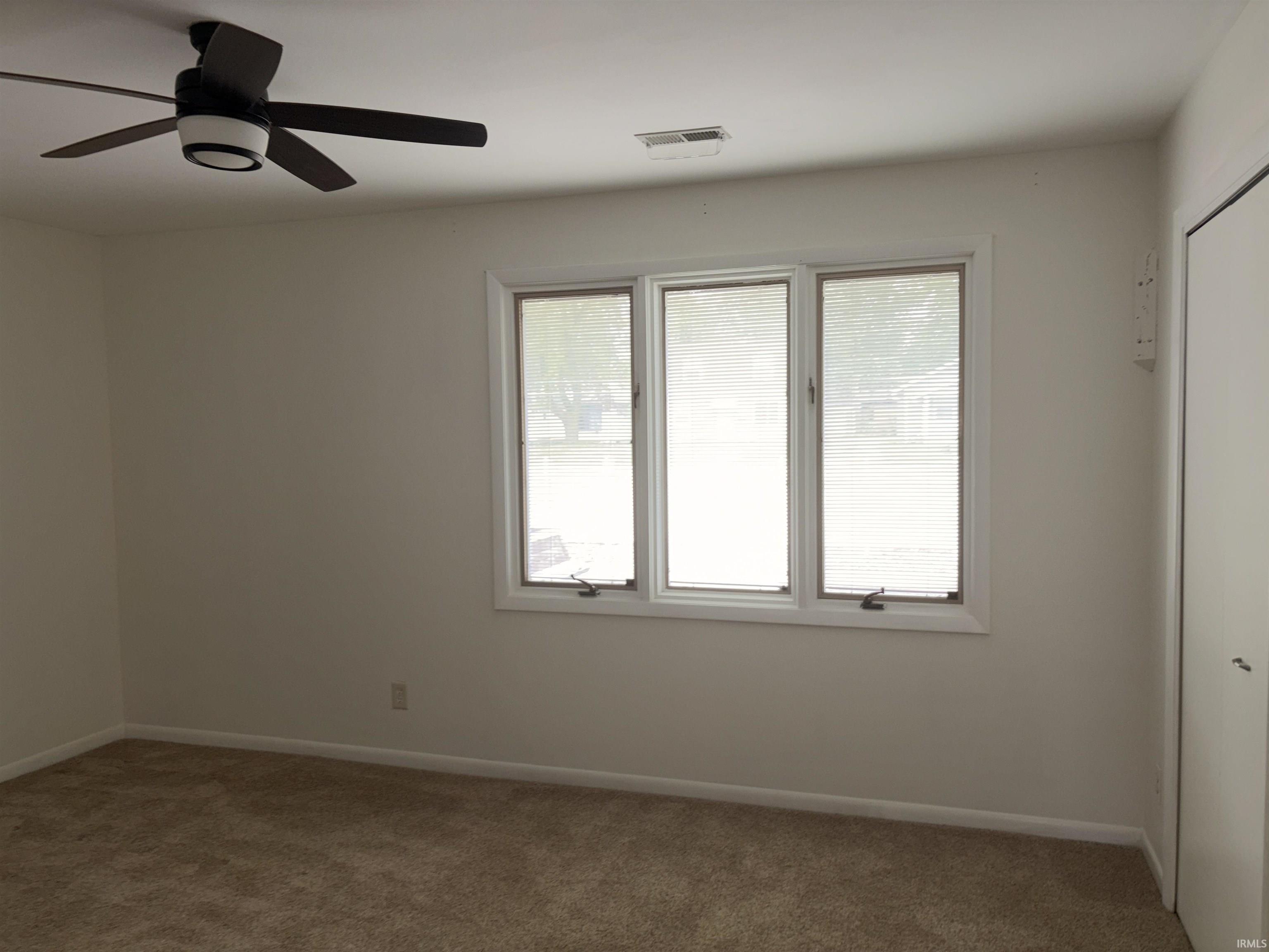 Neutral wall paint, three-pane window, flush-mount ceiling fan with integrated lighting, built-in closet, and carpeted flooring