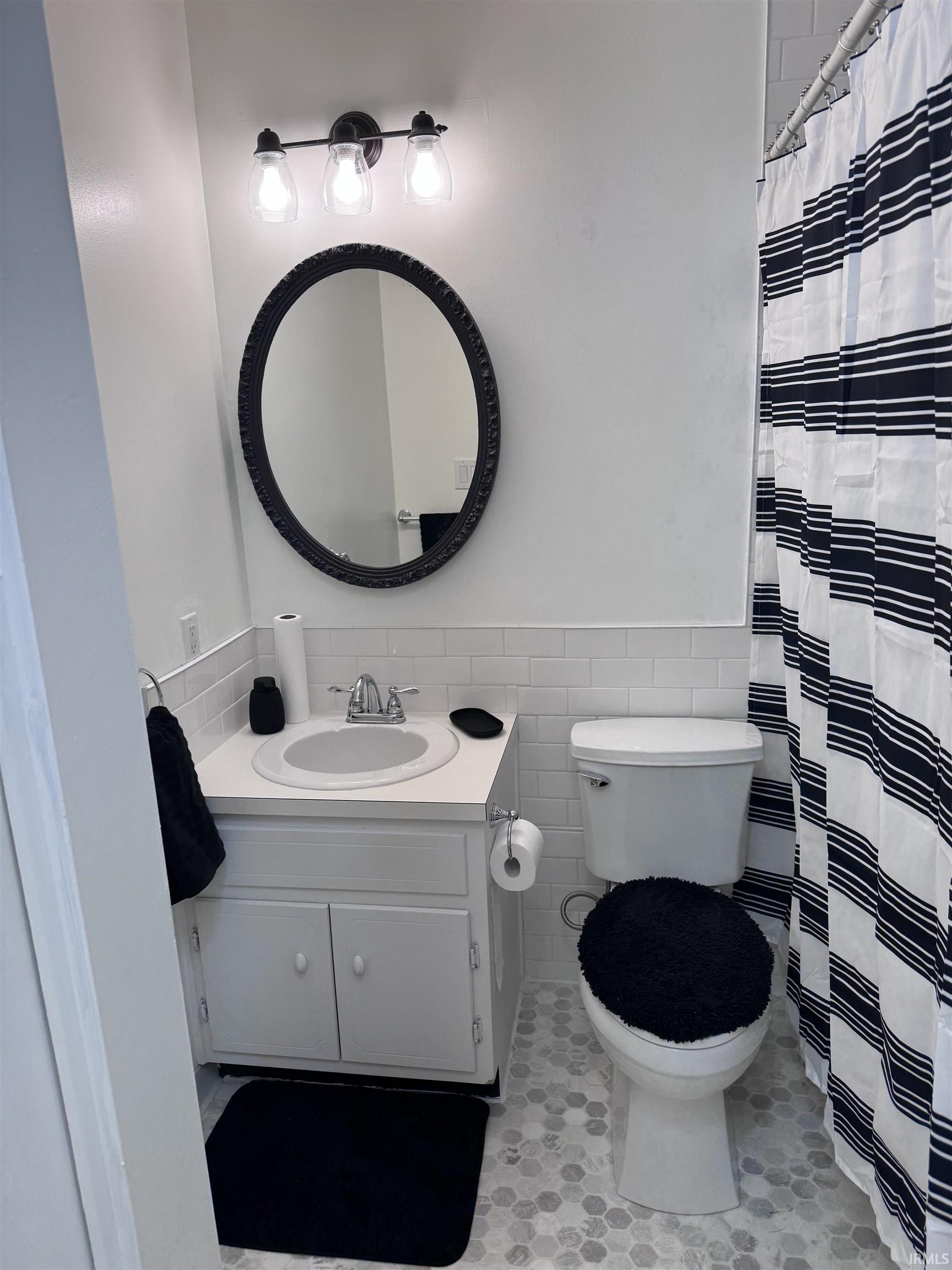 Bathroom featuring a white vanity with integrated sink, chrome faucet, wall-mounted vanity light, an oval mirror, and hexagonal floor tiling