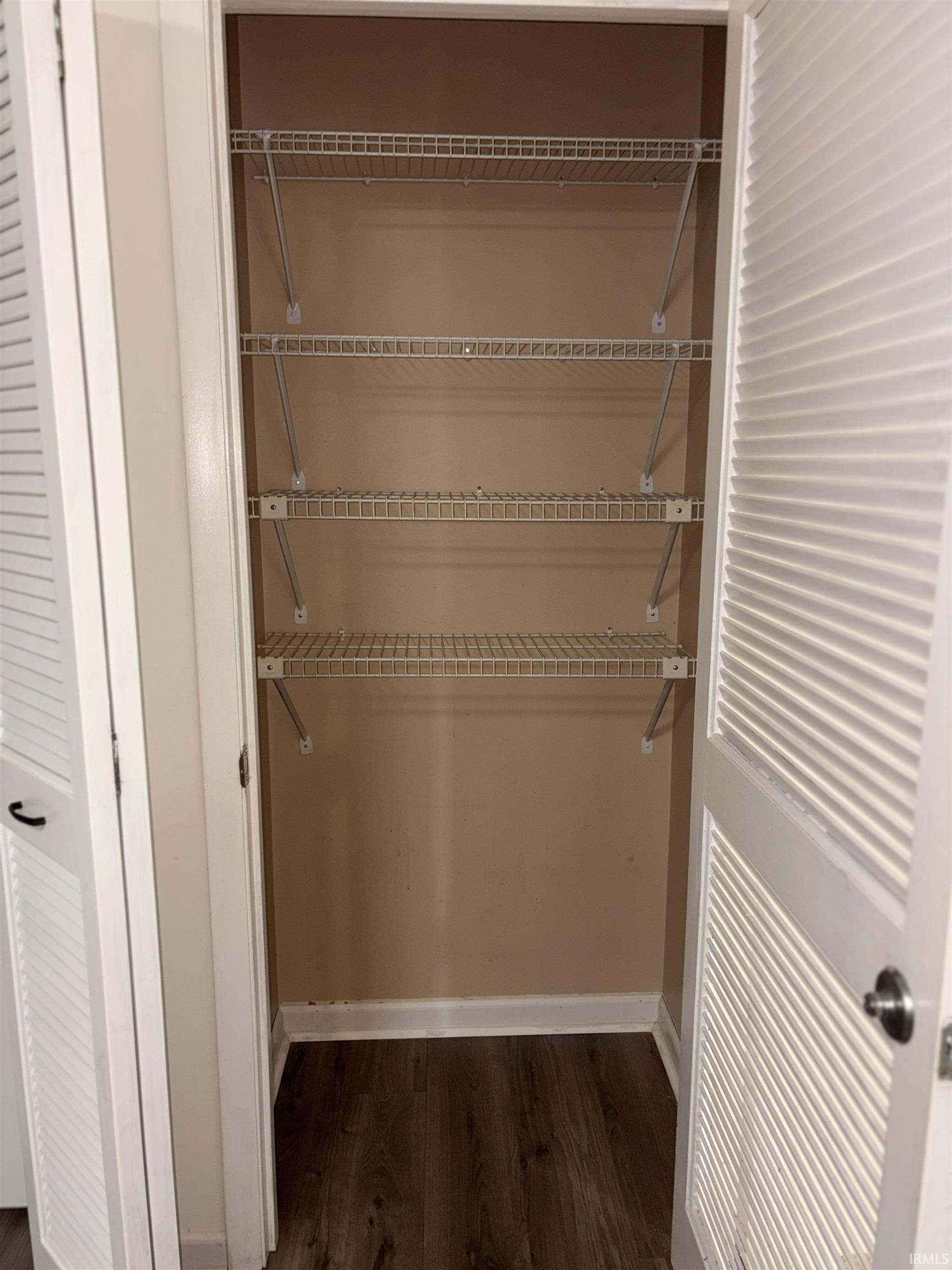 White louvered bi-fold doors opening to a closet with wire shelving and wood-finish flooring