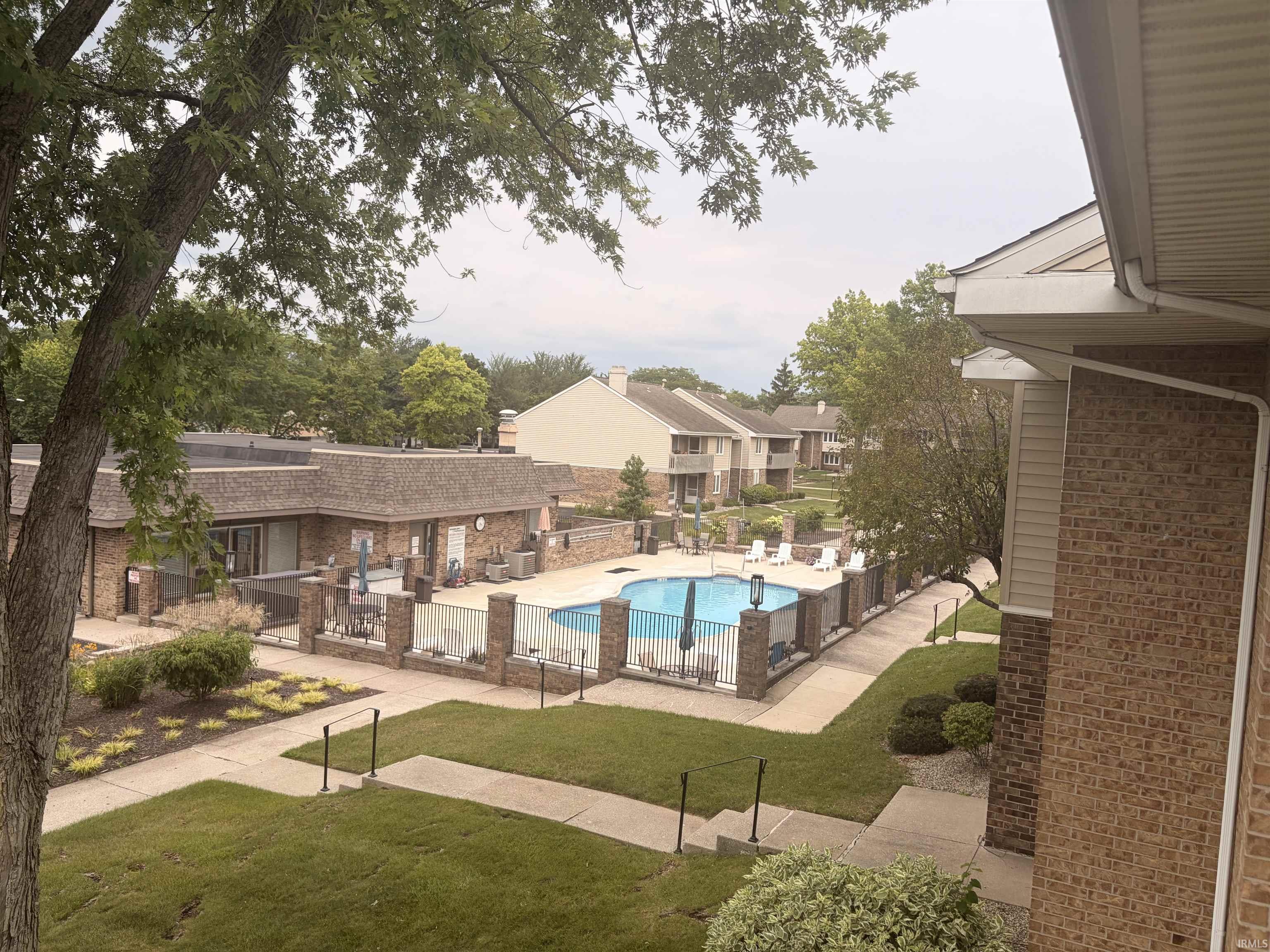 Community pool with surrounding patio, brick-clad buildings, paved walkways, and landscaped grounds