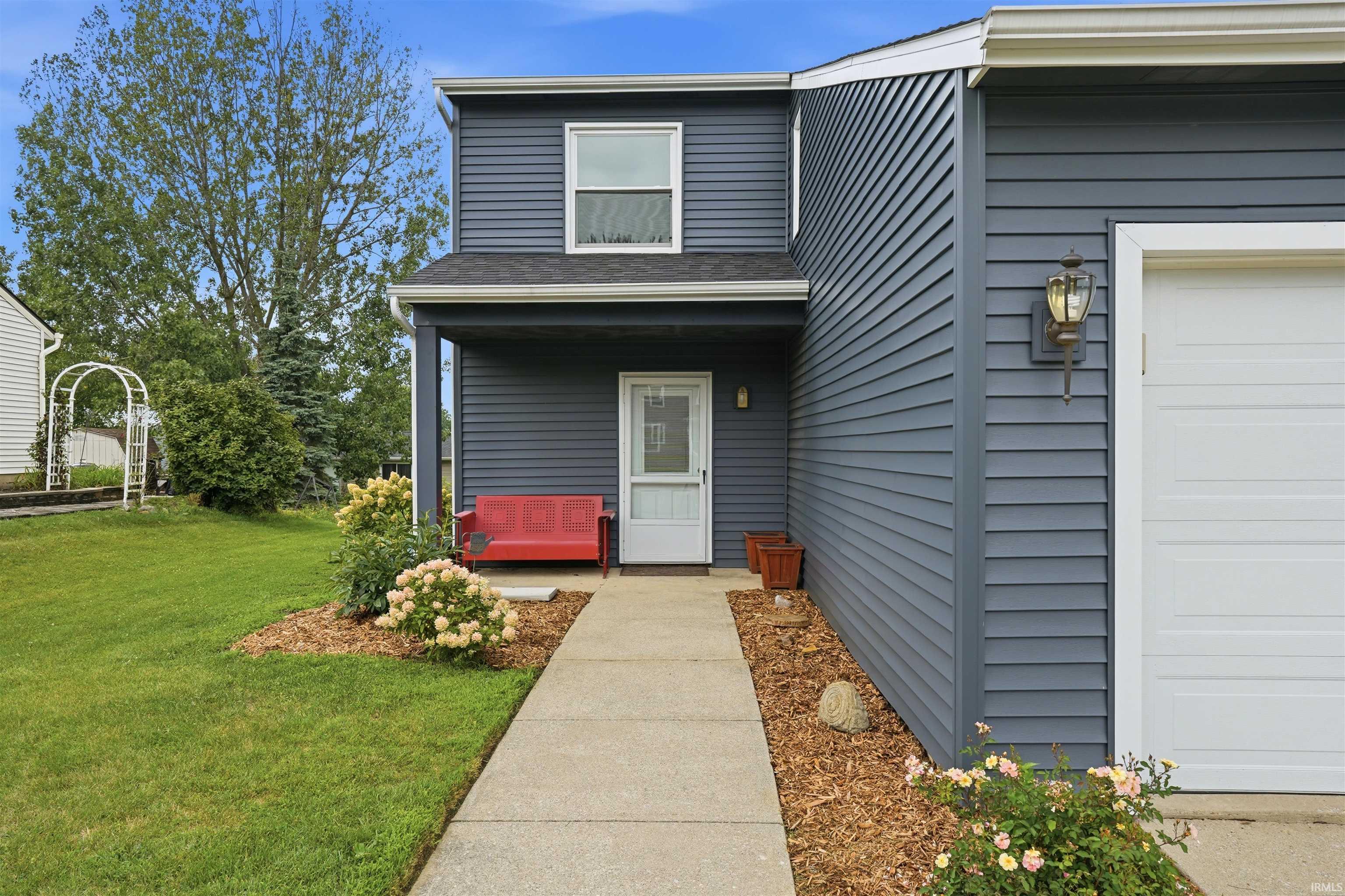 Modern two-story home featuring charcoal fiber cement siding, a welcoming front entry with white door surround, and a mature landscaped lawn with flowering plantings along the foundation