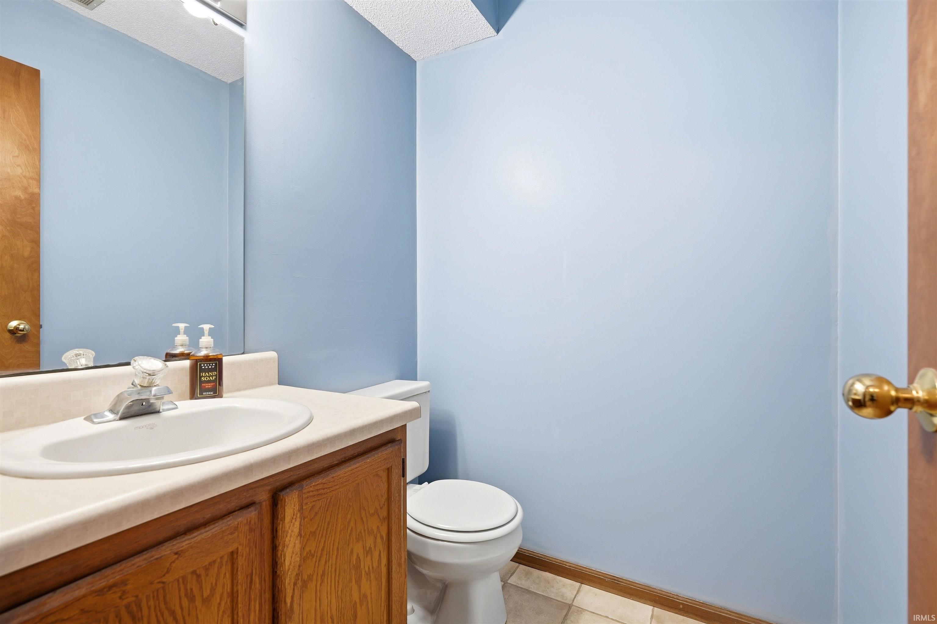 Bright half-bath featuring a wood-finish vanity with an integrated sink, ceramic tile flooring, and soft blue painted walls