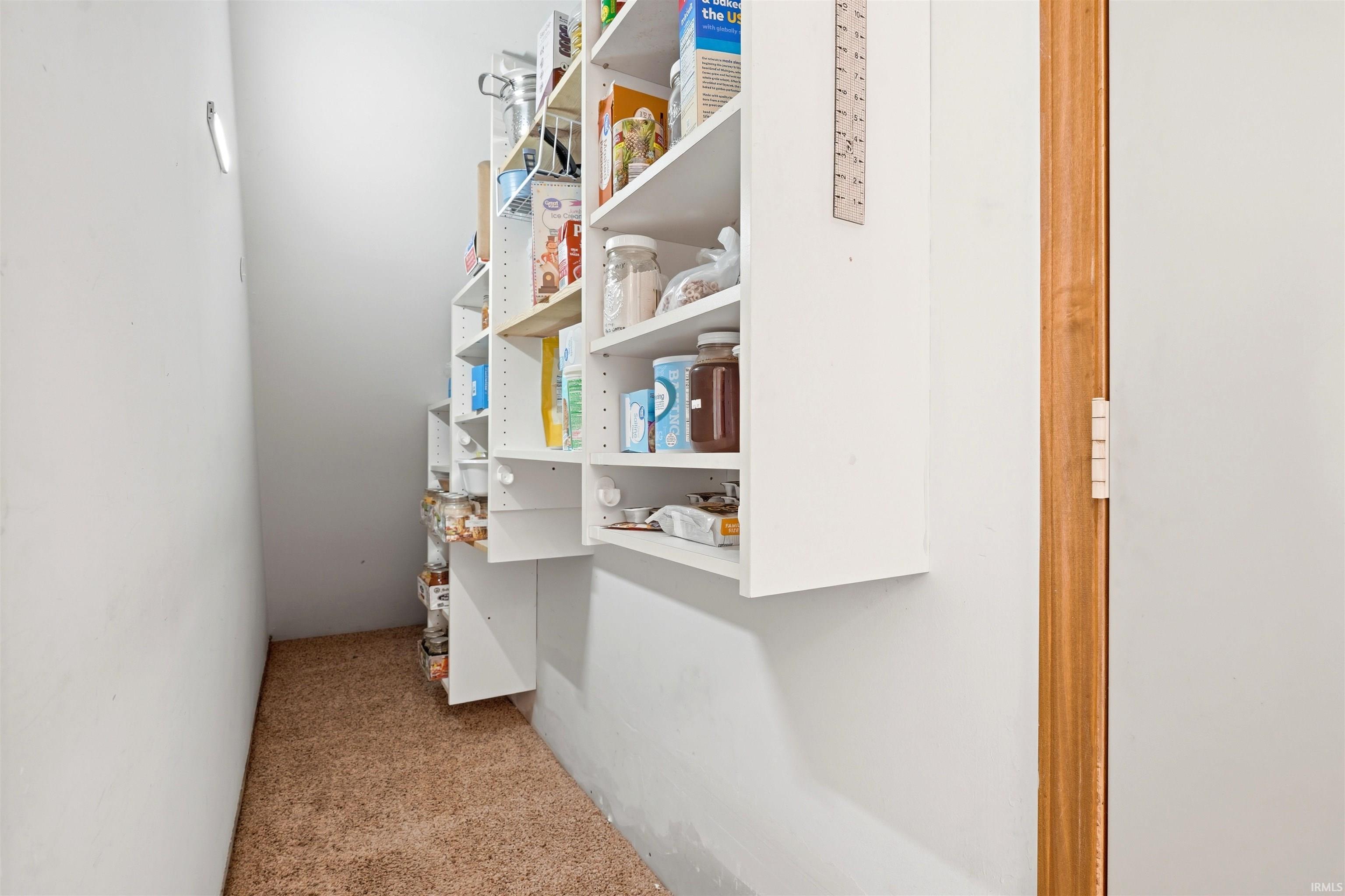 Efficient pantry storage featuring built-in white cabinetry with multiple shelves, cork flooring, and organized shelving for pantry staples and household essentials